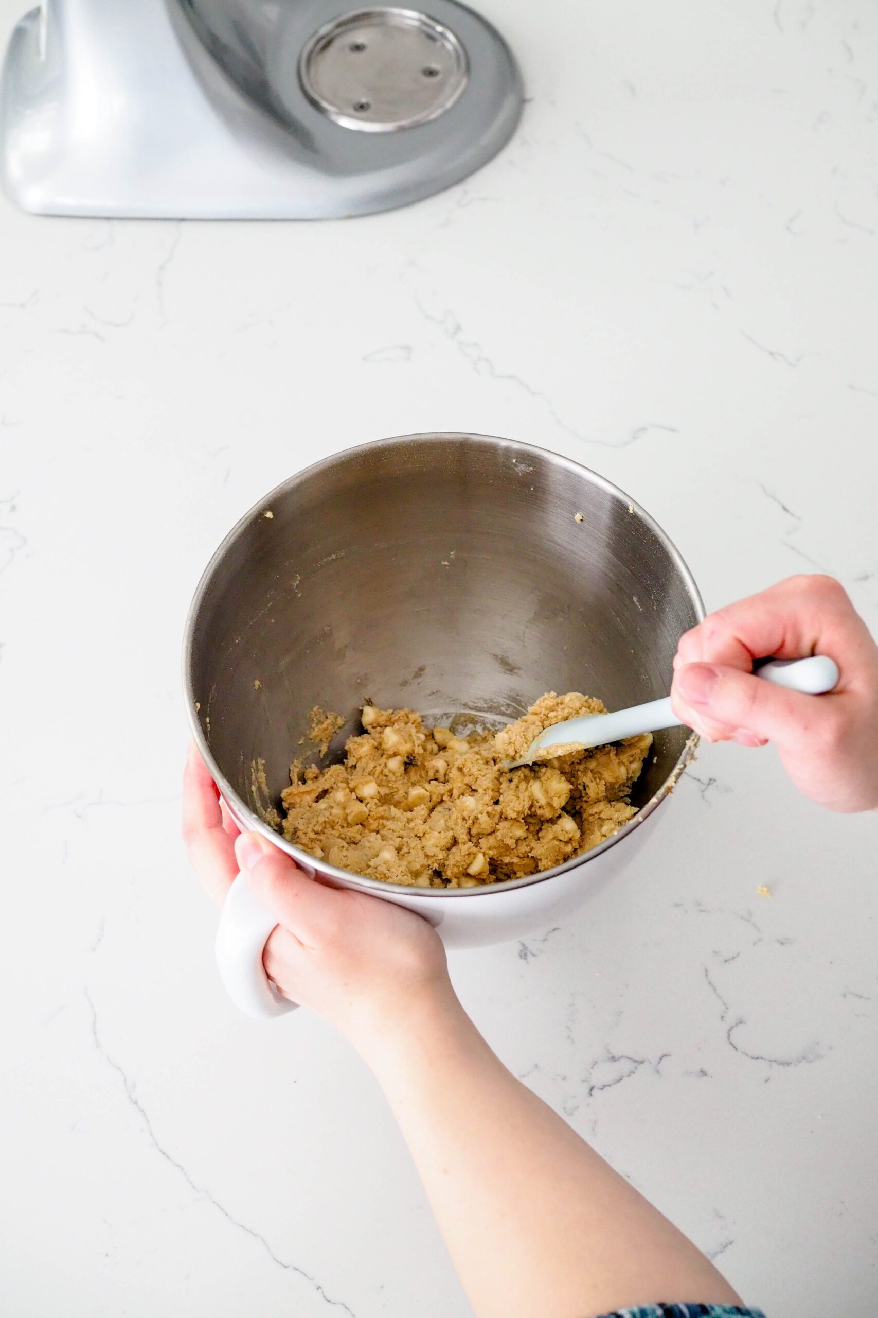 A hand stirs together white chocolate chips and lavender cookie dough.