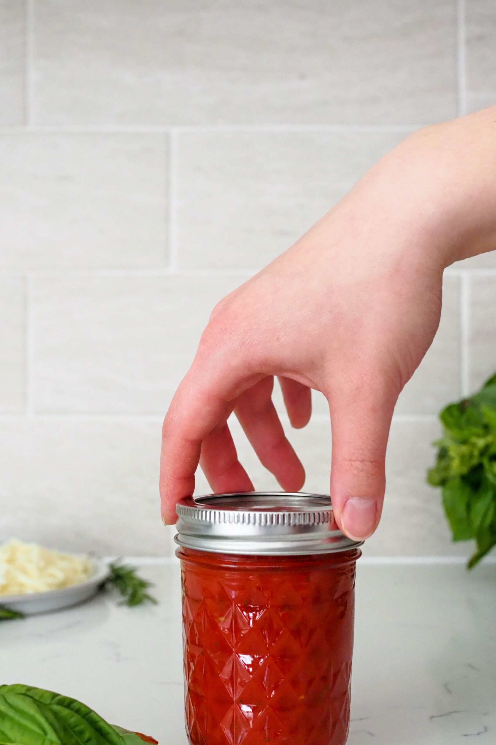 A hand screws on the lid of a jar containing pizza sauce made from tomato paste.