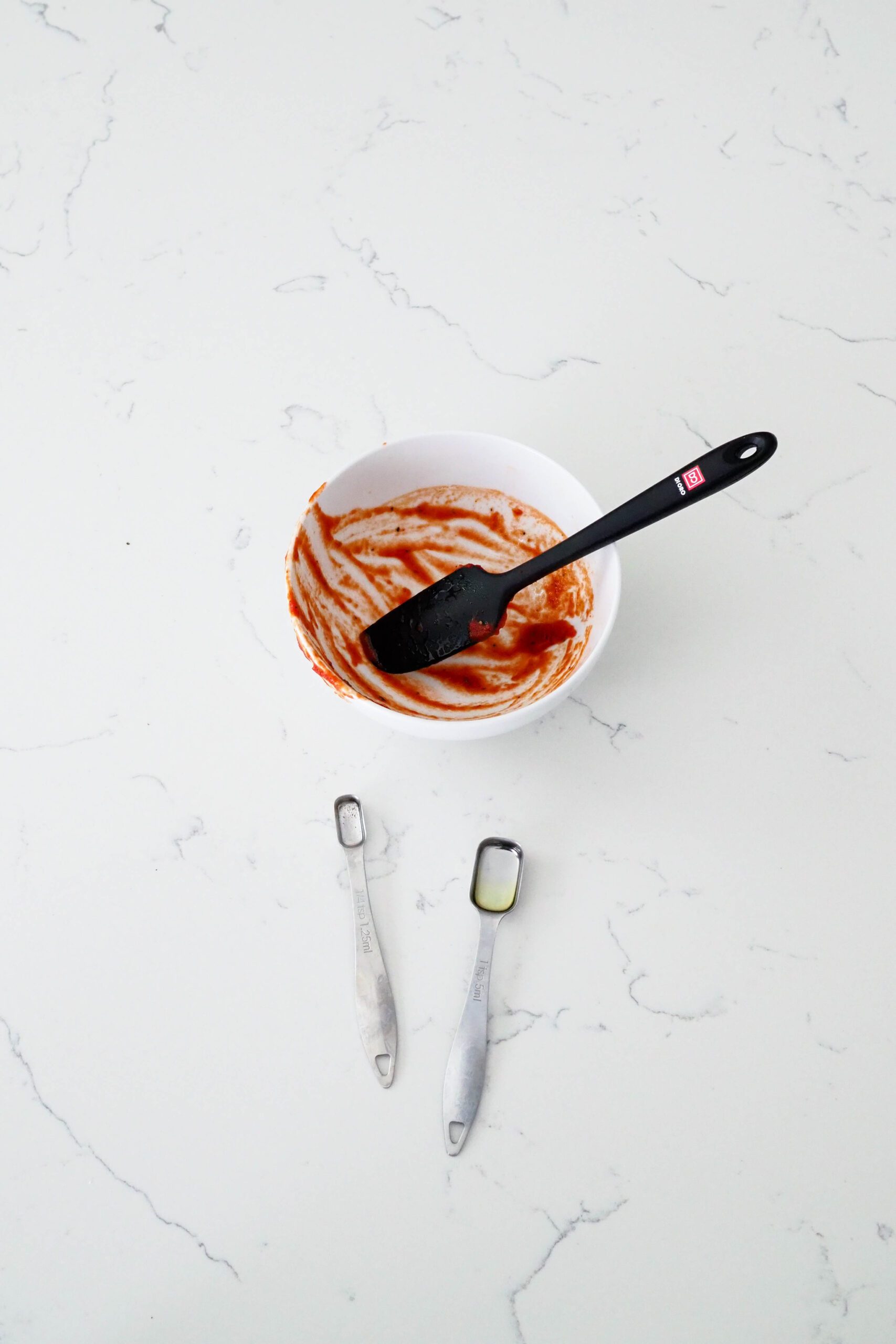 A single bowl, spatula, and two measuring spoons on a quartz counter.