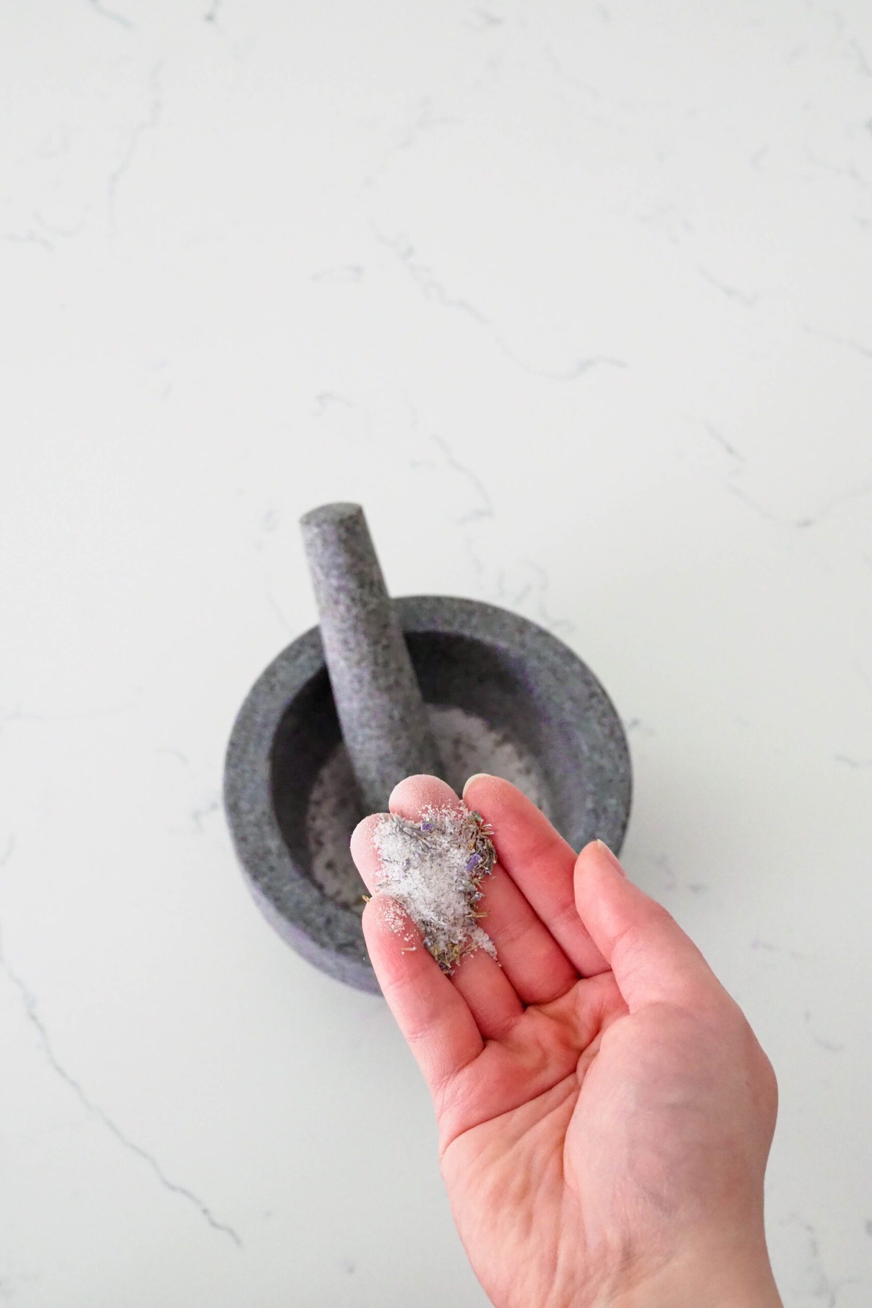 A hand holds up lavender sugar, which has been ground together in a mortar and pestle.