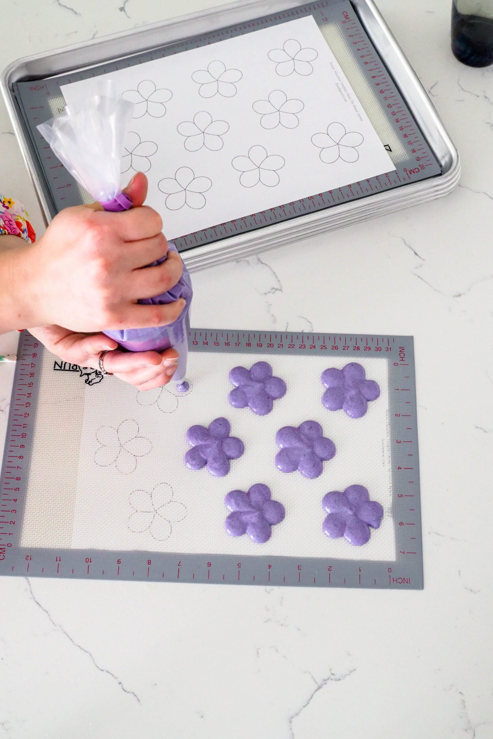 A hand pipes flower-shaped macarons onto a silicone mat.