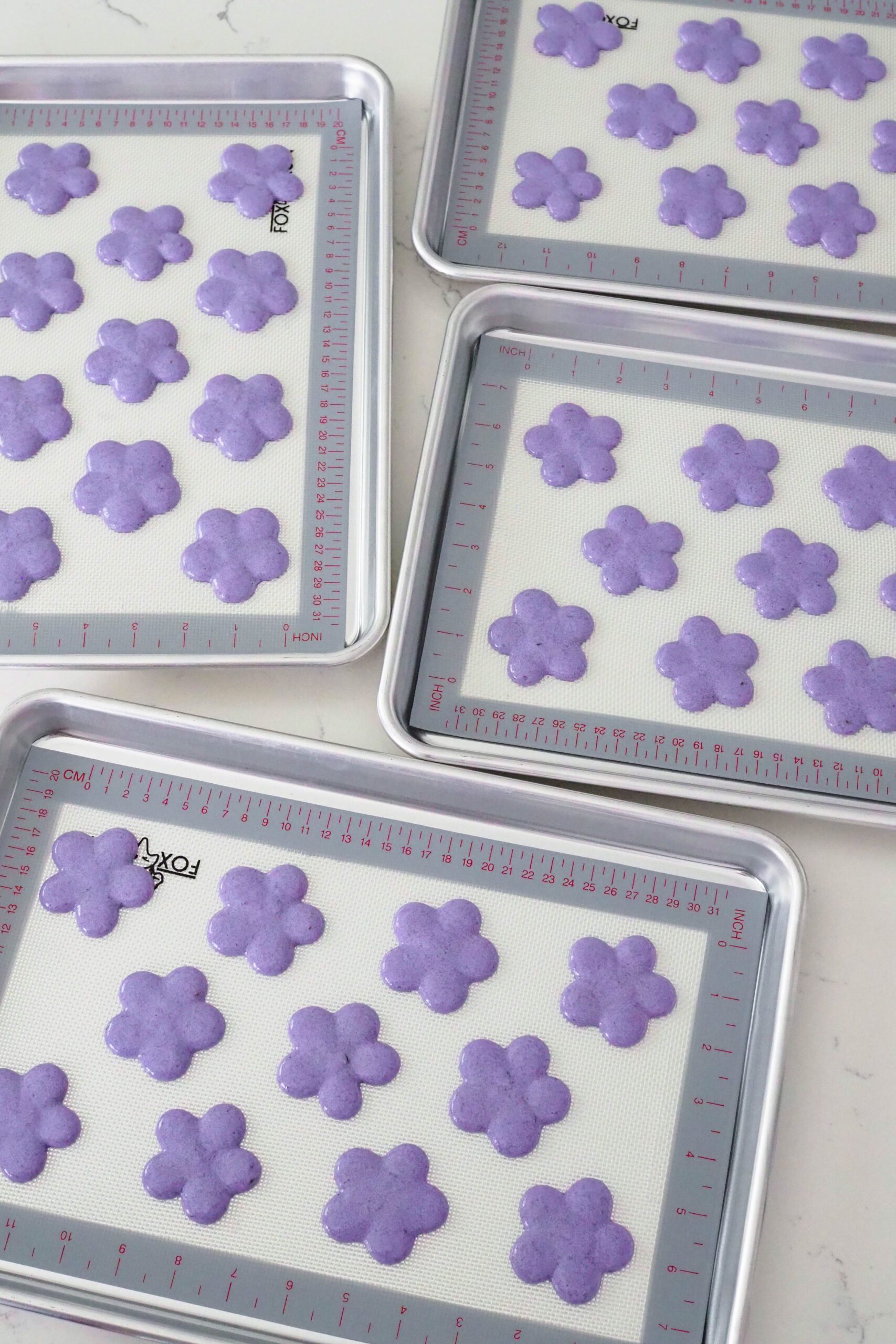 Piped flower macaron shells rest before baking.