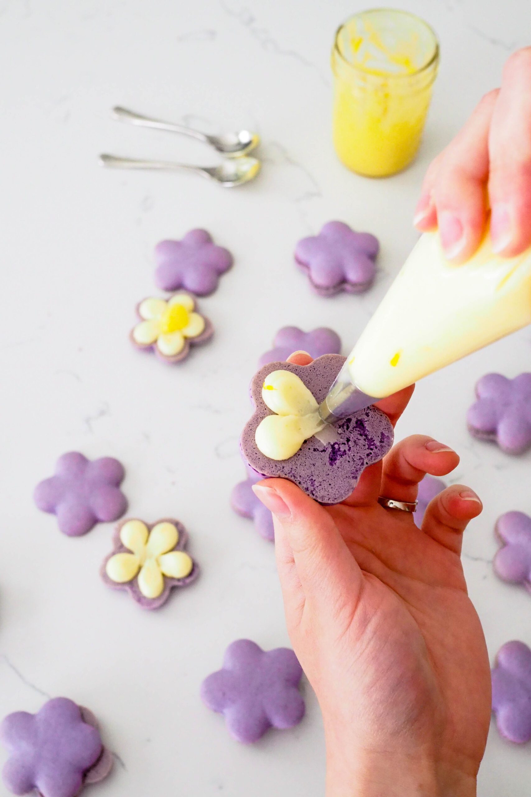 A piping tip pipes circles on the underside of a flower-shaped macaron.