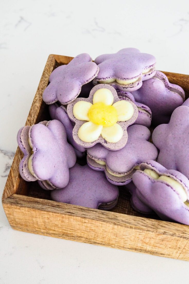 Purple flower-shaped macarons stacked high in a wooden box.