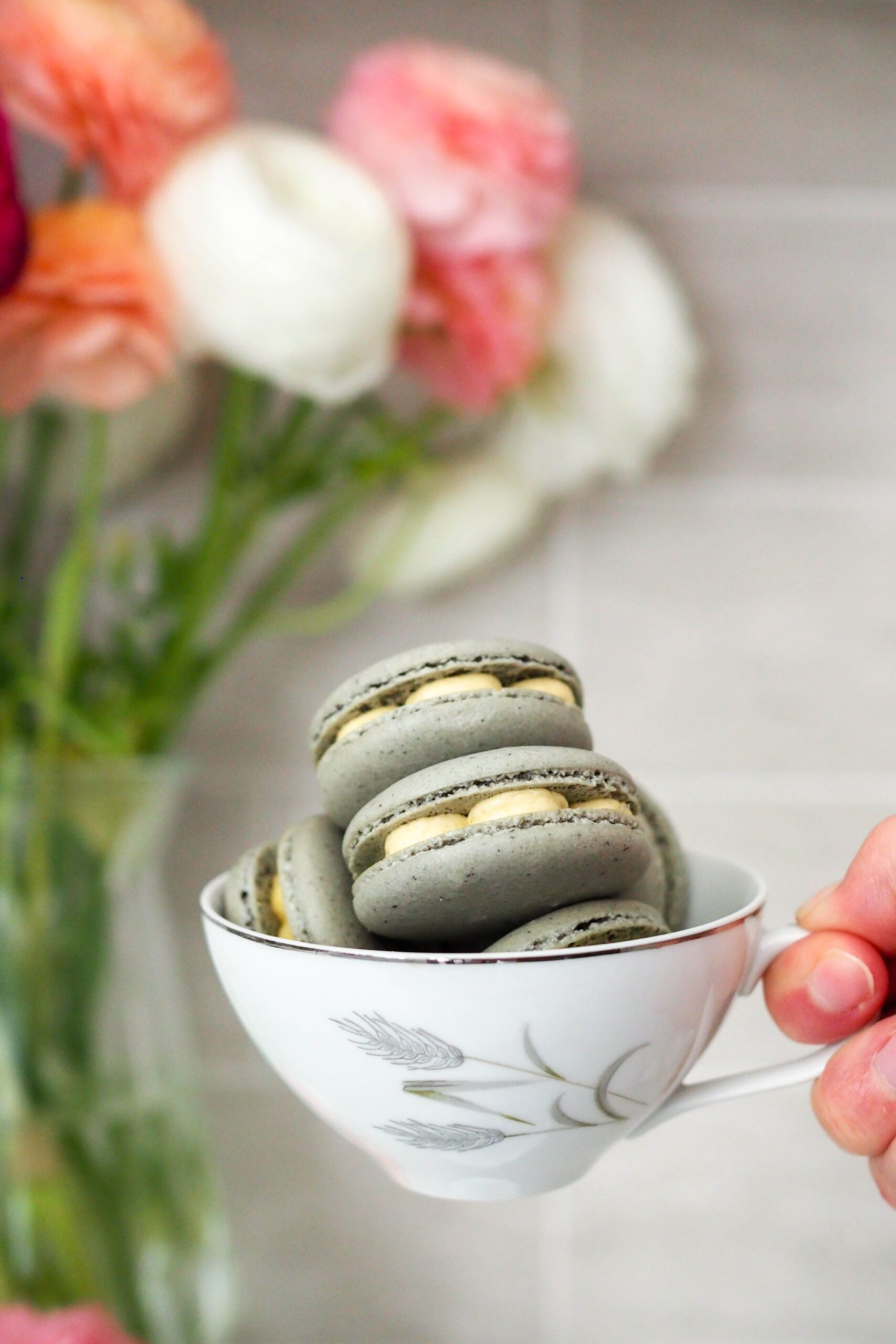 A hand holds up a teacup full of macarons.