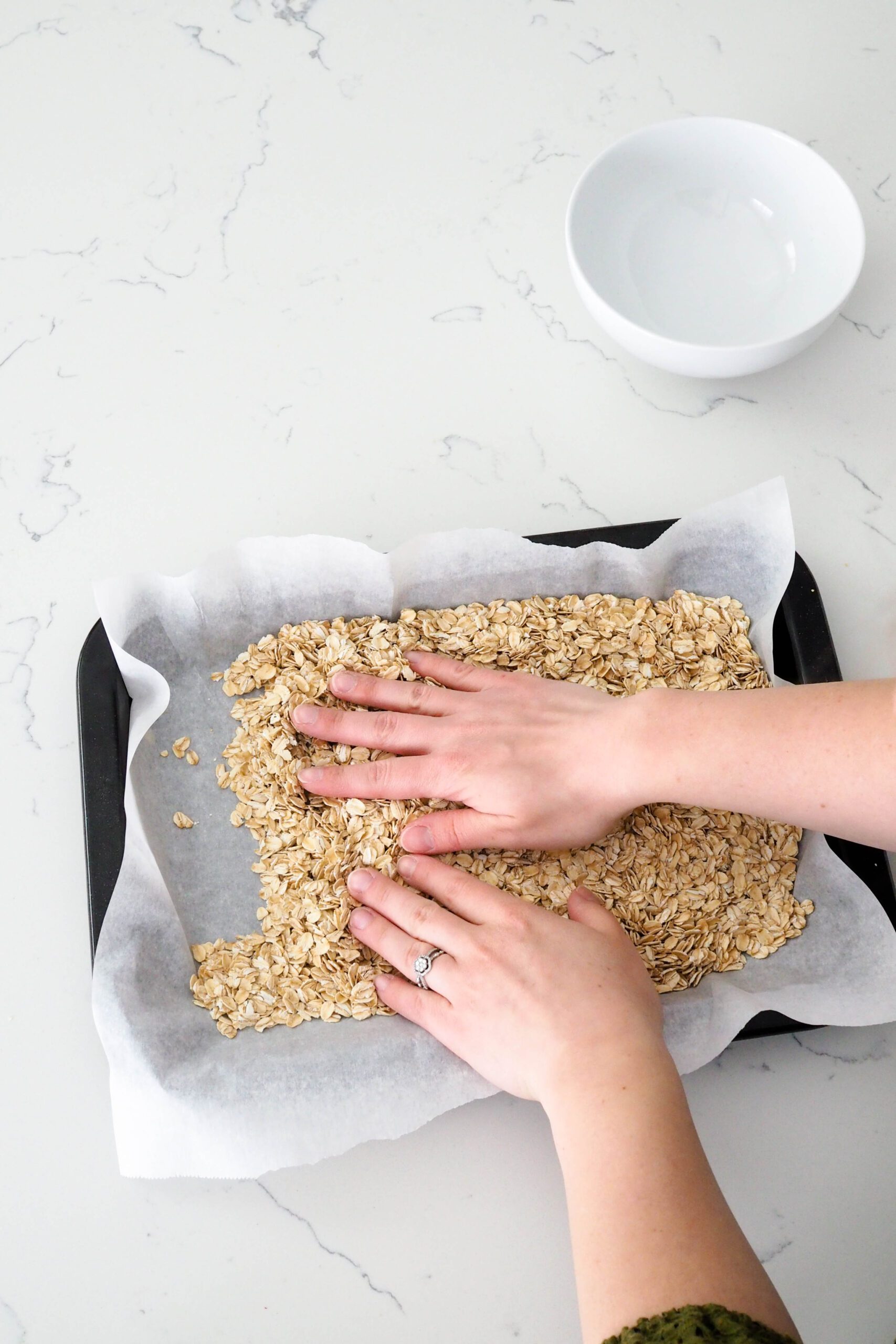 Two hands spread oats onto a baking sheet.