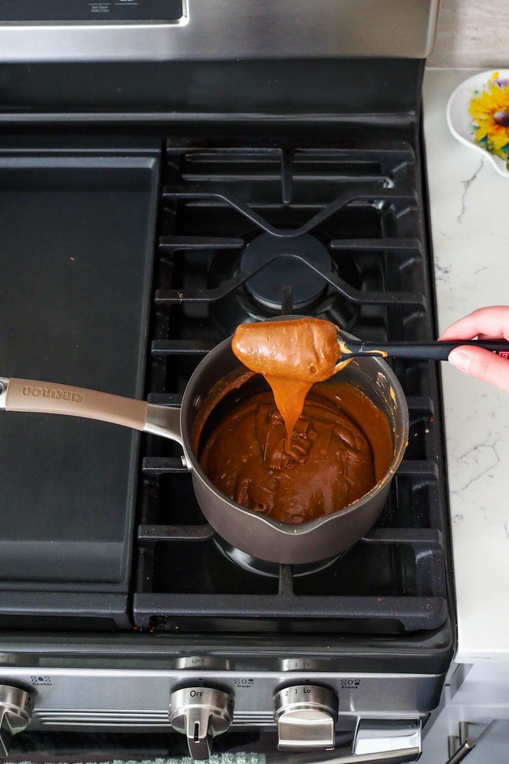 A spatula drizzles melted peanut butter, milk, and protein powder off of a spatula.