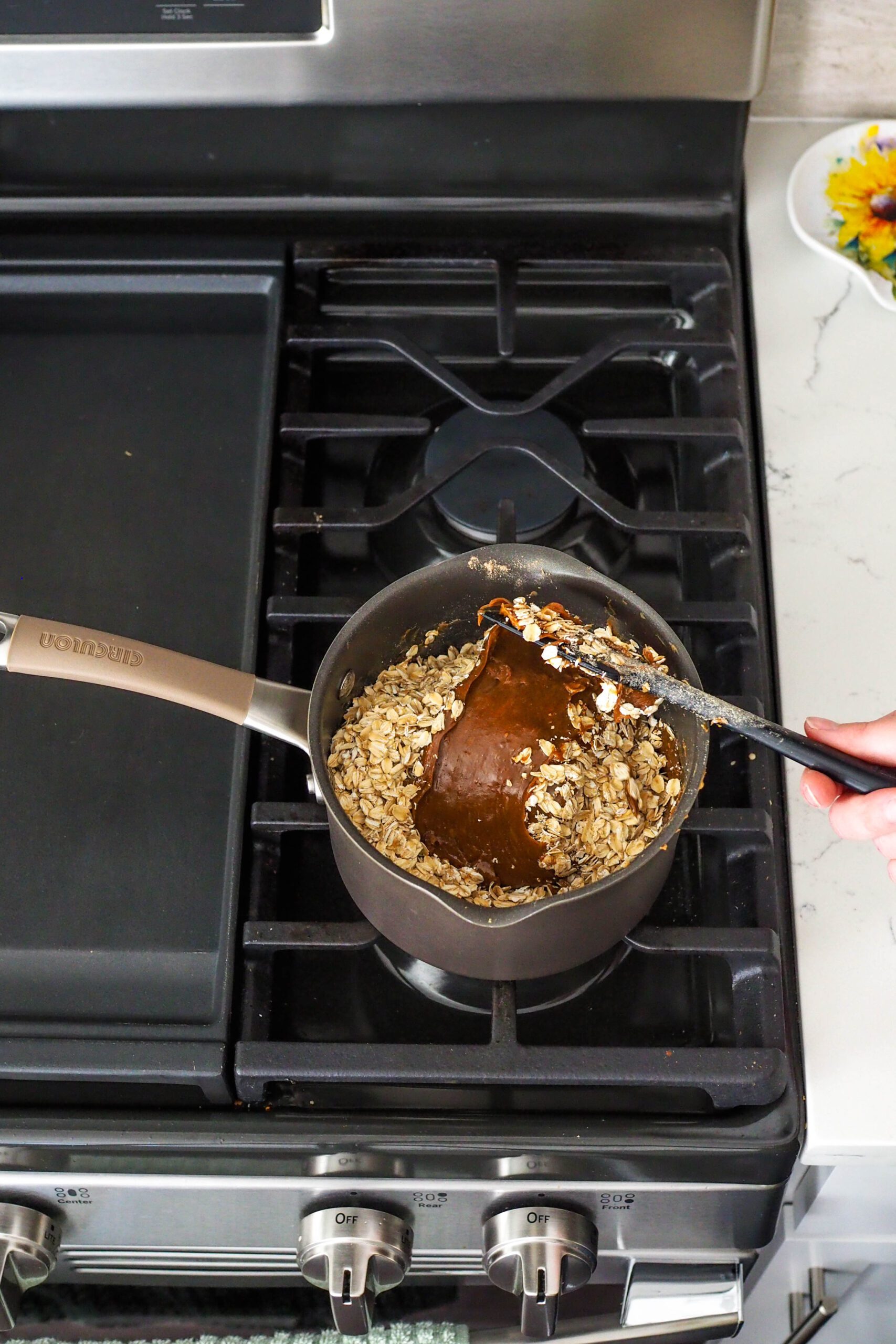 A spatula folds oats into a dark brown peanut butter and protein powder mixture.