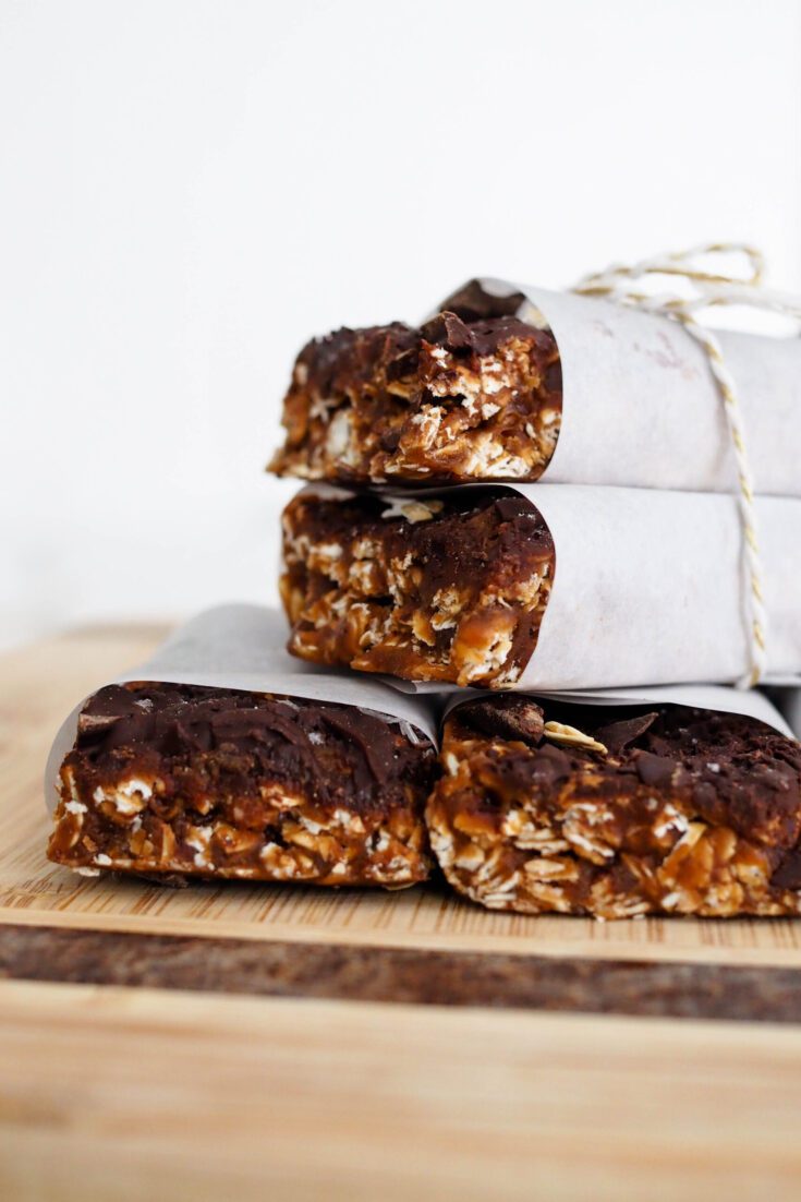 A stack of chocolate no-bake protein granola bars on a wooden cutting board.