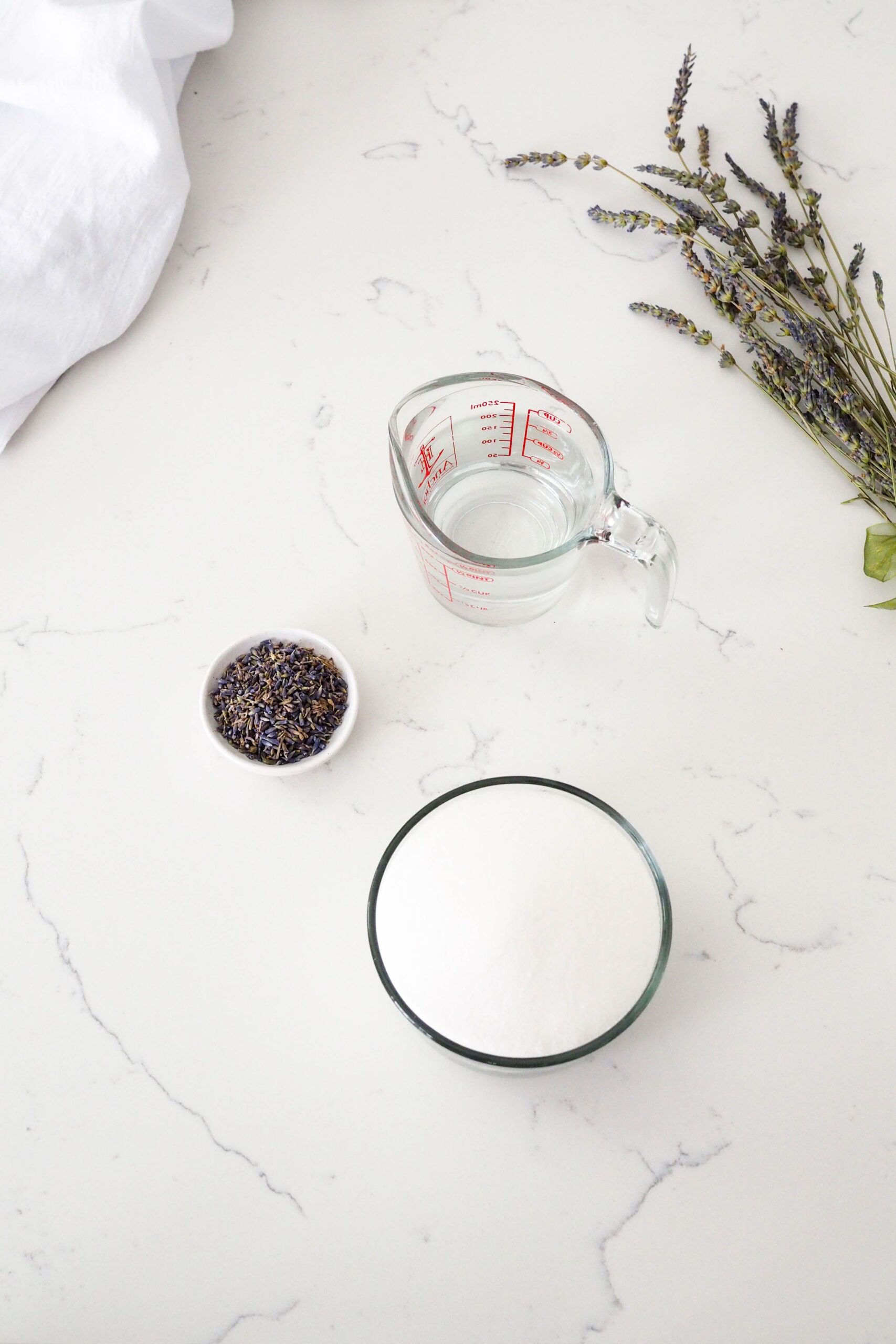 Water, sugar, and lavender buds on a counter.