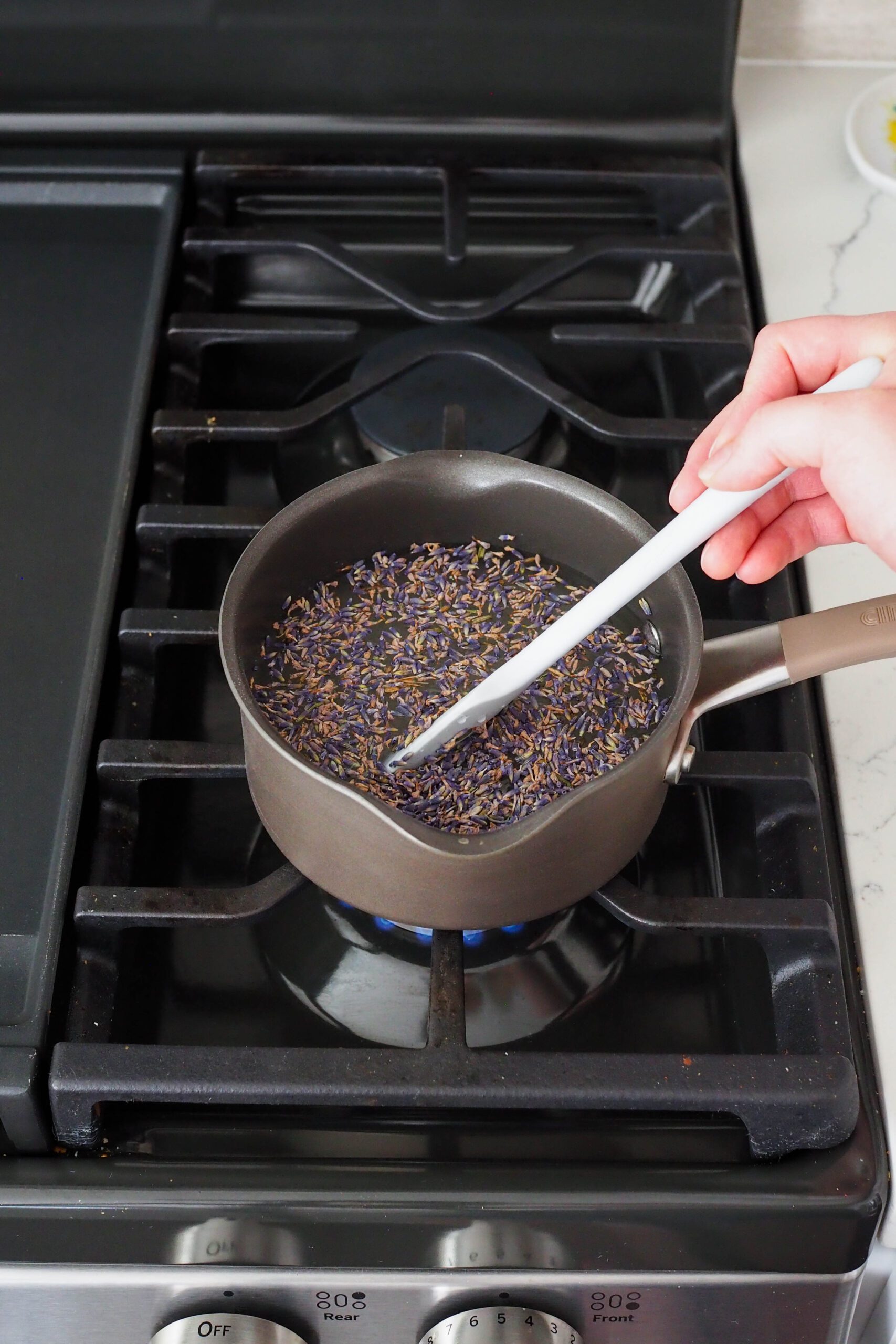 A hand stirs lavender simple syrup in a saucepan over medium heat.