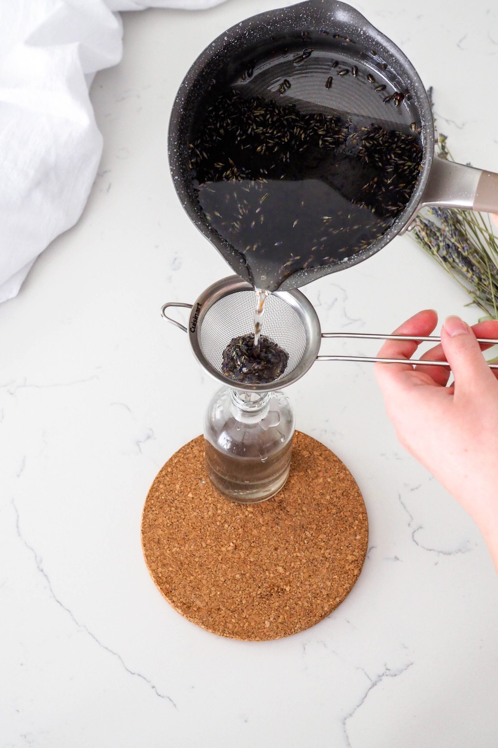 Lavender syrup is poured through a fine mesh strainer into a narrow-necked bottle.