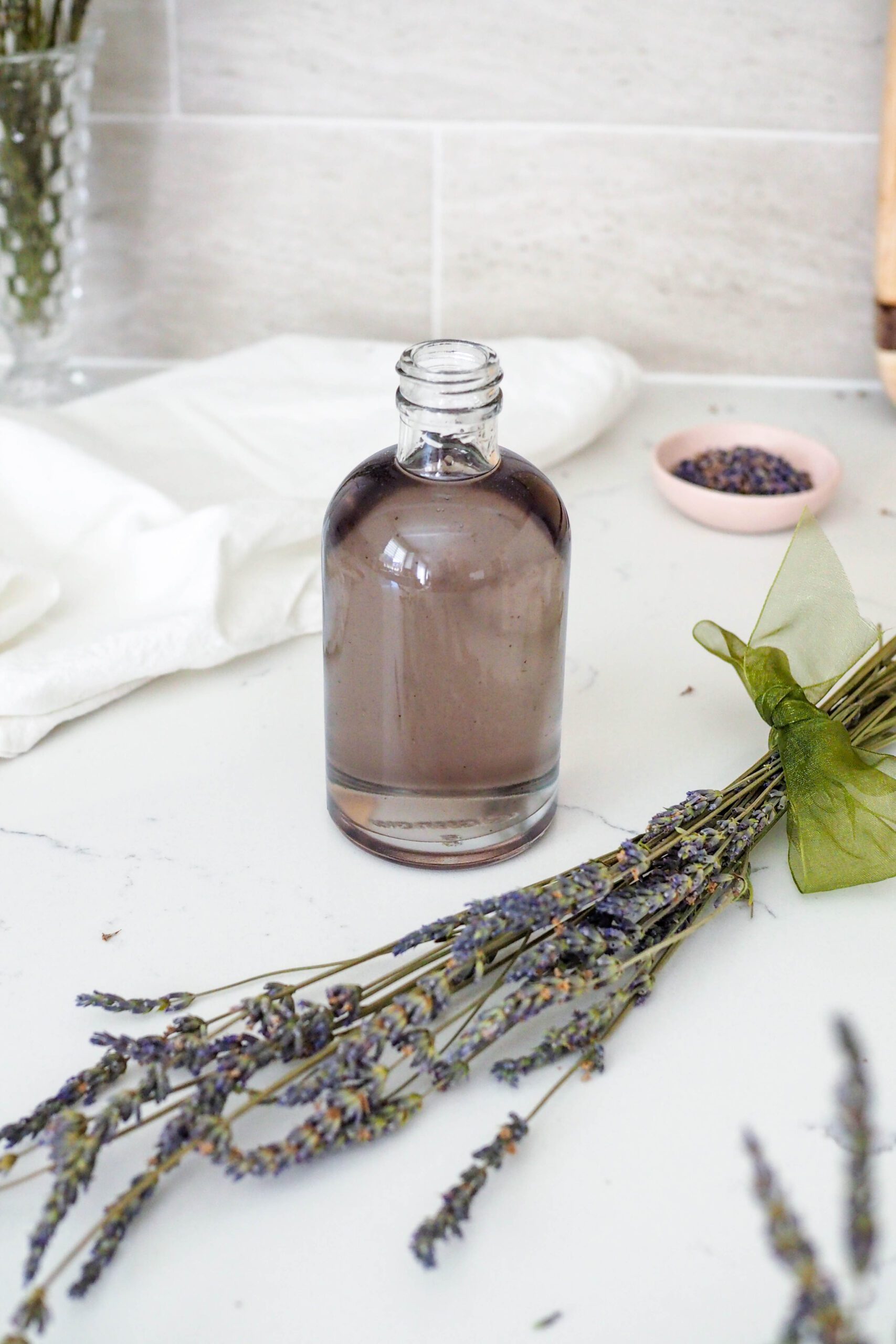 A bottle of lavender simple syrup on a counter near dried lavender sprigs.