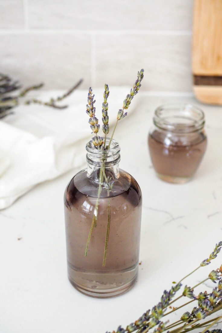 Three lavender sprigs stick out of a bottle of lavender syrup.