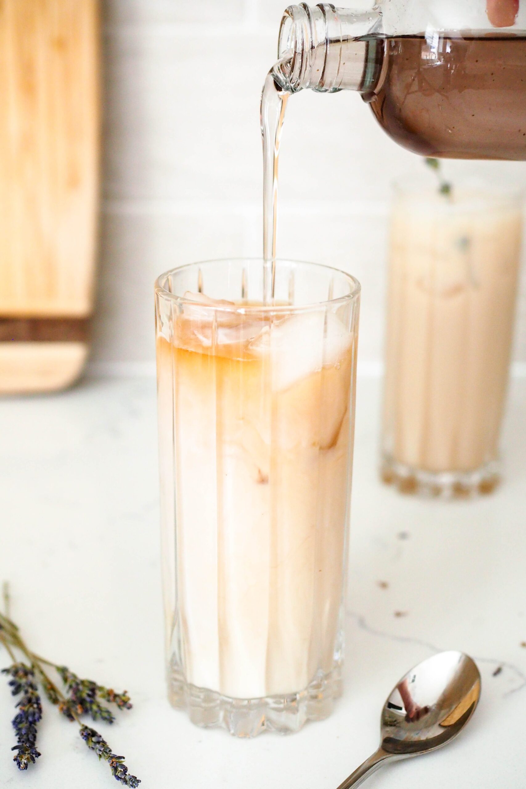 A bottle pours lavender syrup into an iced tea latte.