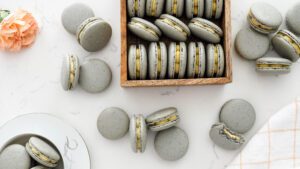 A wooden box of grey macarons is surrounded by more macarons.