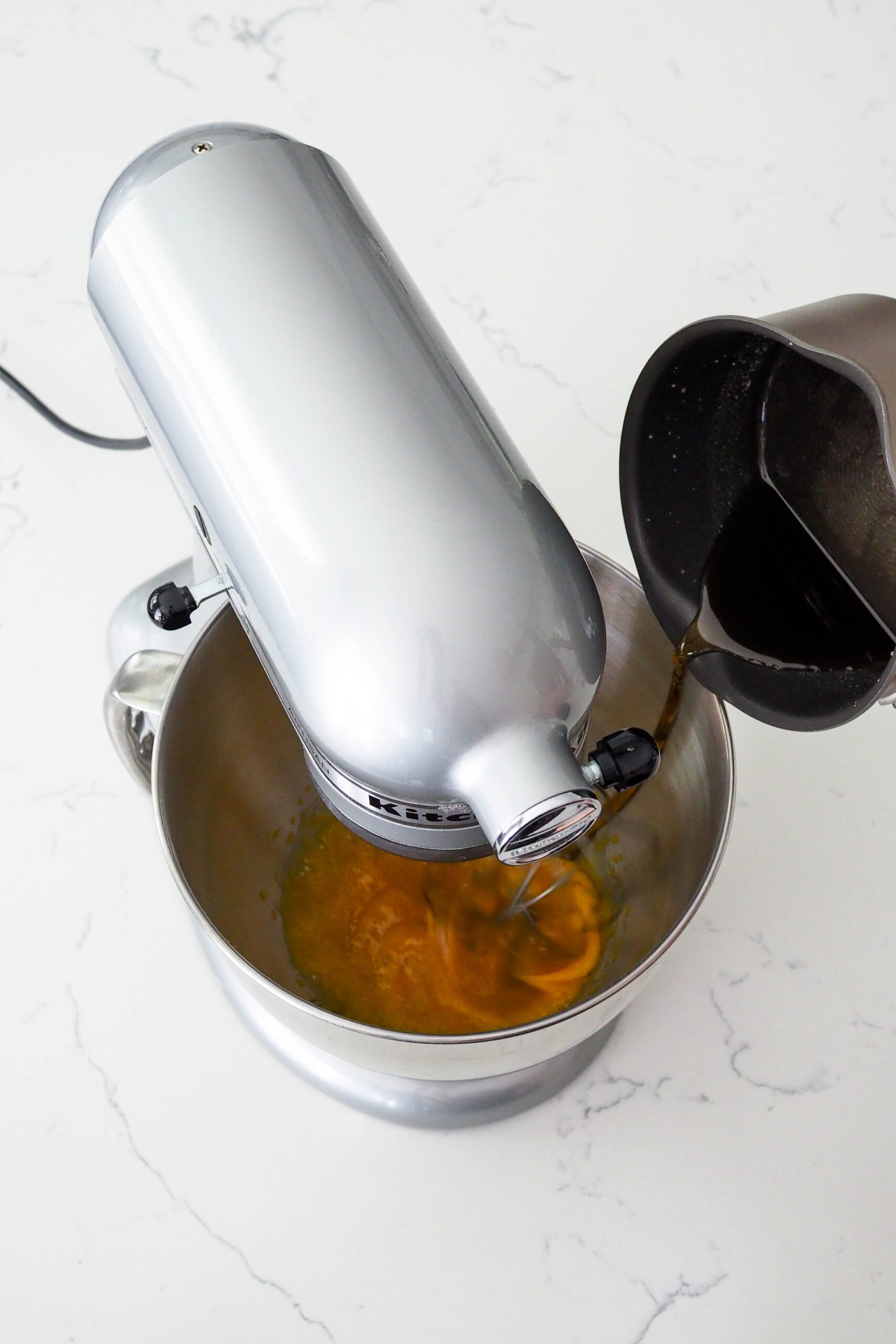 Sugar is poured into a stand mixer bowl from a saucepan.