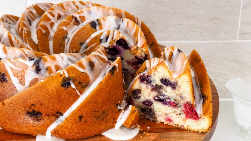 A slice is being removed from a berry Bundt cake on a cake stand.