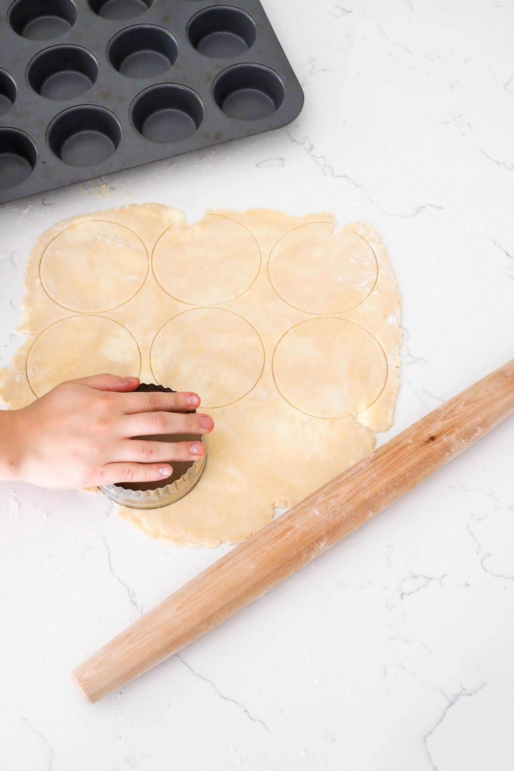A hand cuts circles out of a rolled out pie crust.