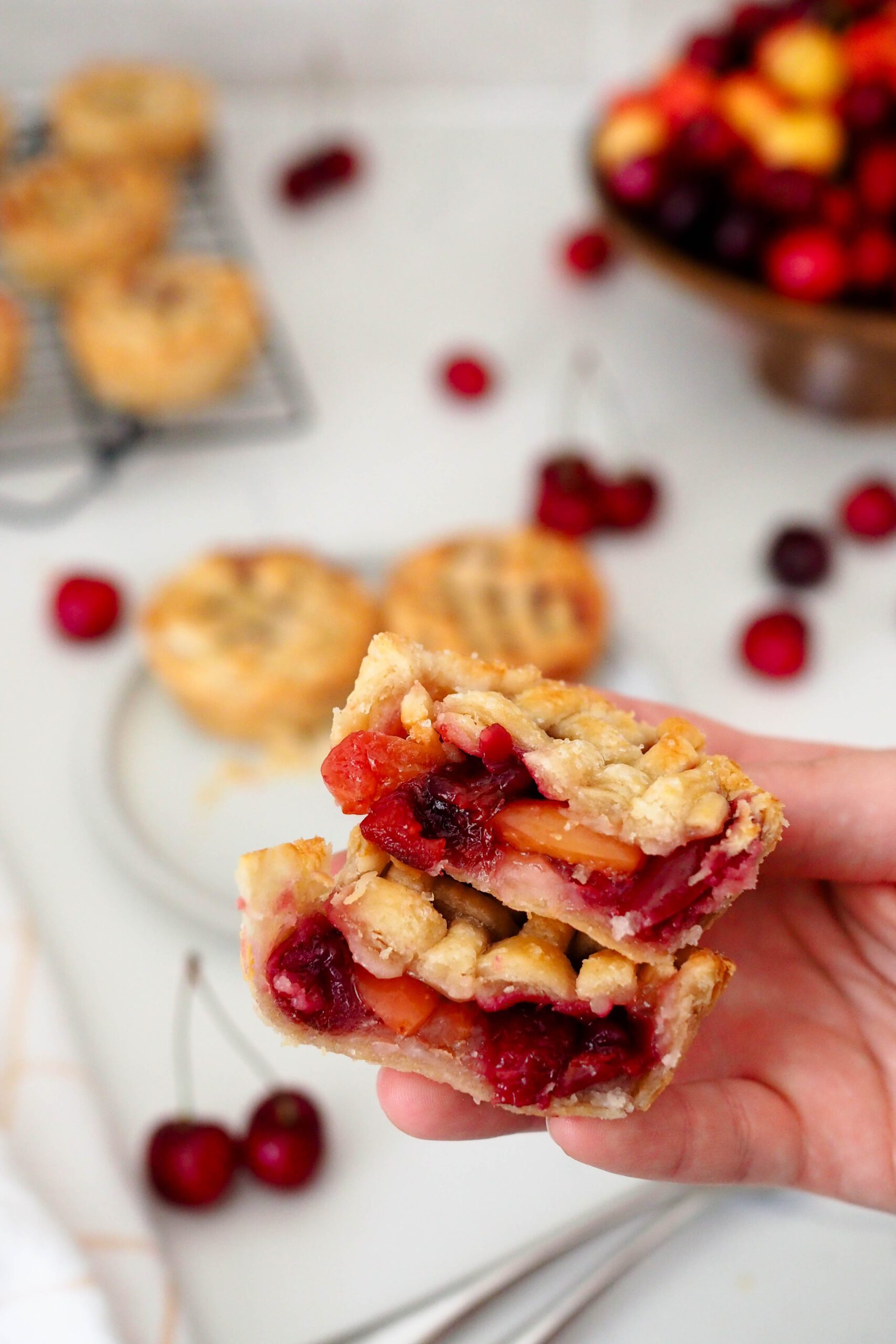 A hand holds up two halves of a mini cherry pie.