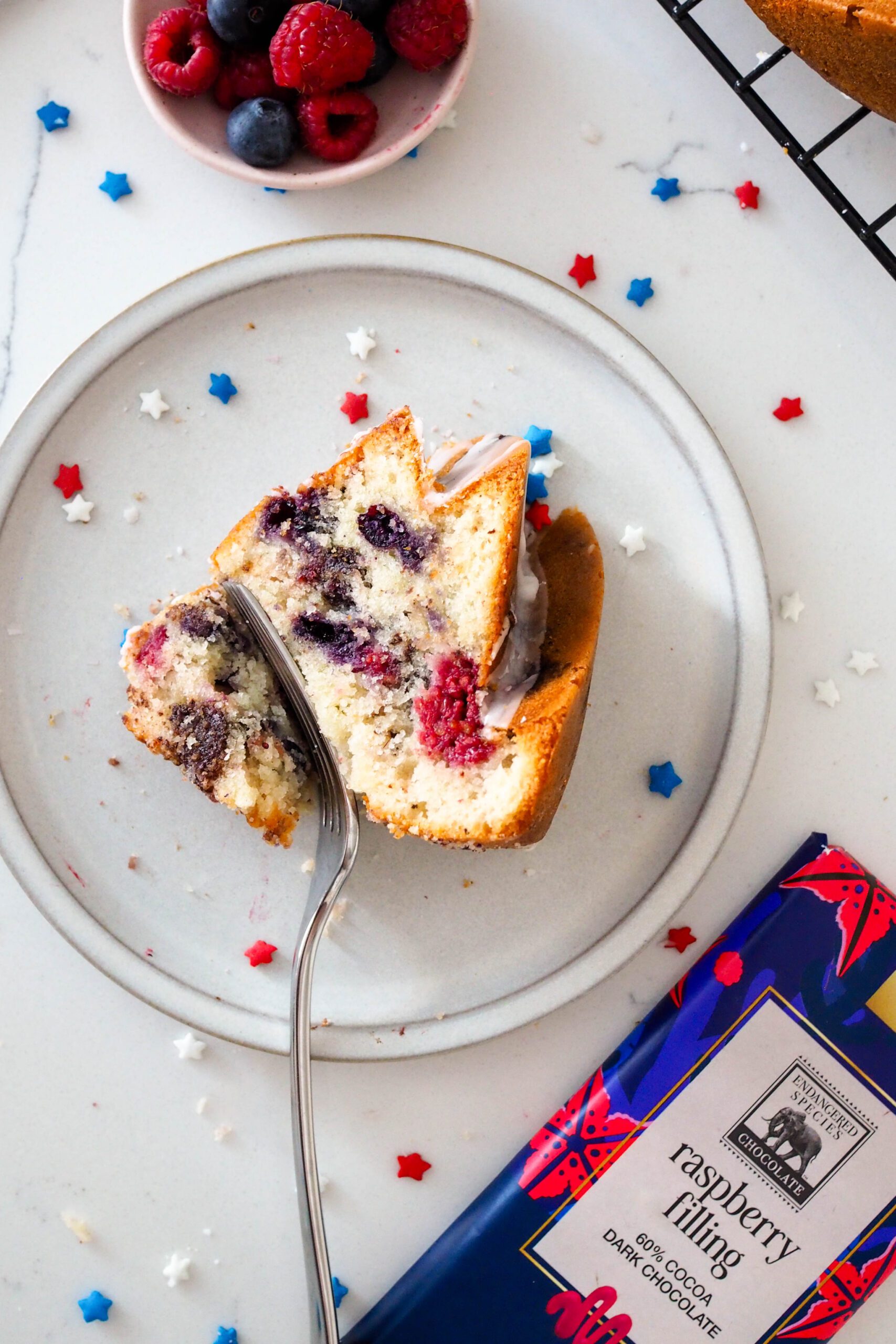 A slice of berry Bundt cake on a grey plate with red, white, and blue sprinkles around it.
