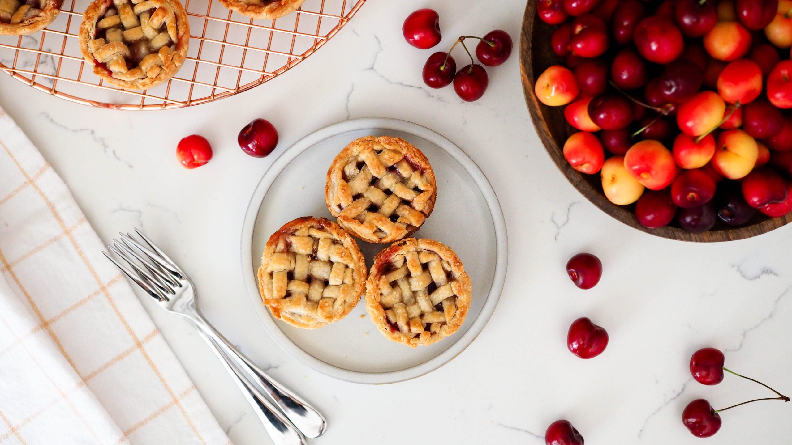 A plate with three mini cherry pies surrounded by cherries.