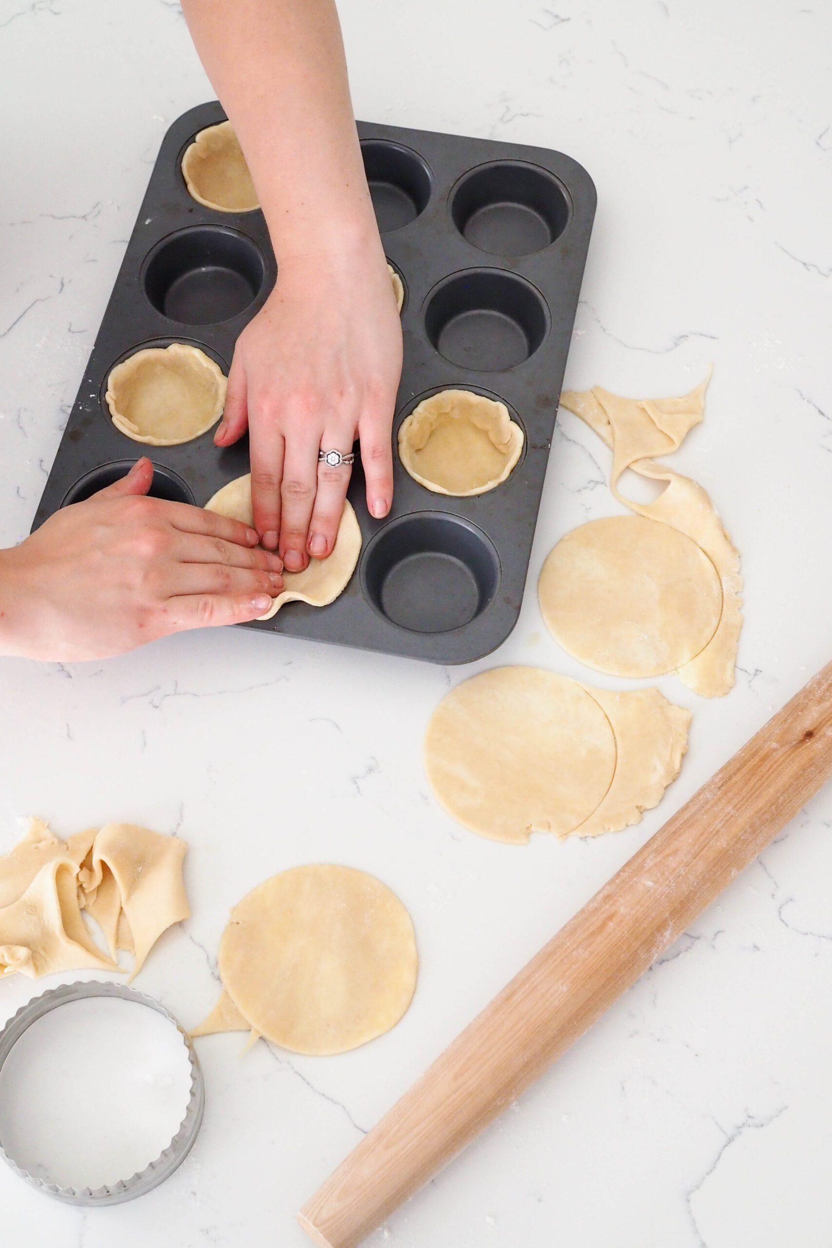 Two hands press a circle of pie dough into a muffin pan opening.