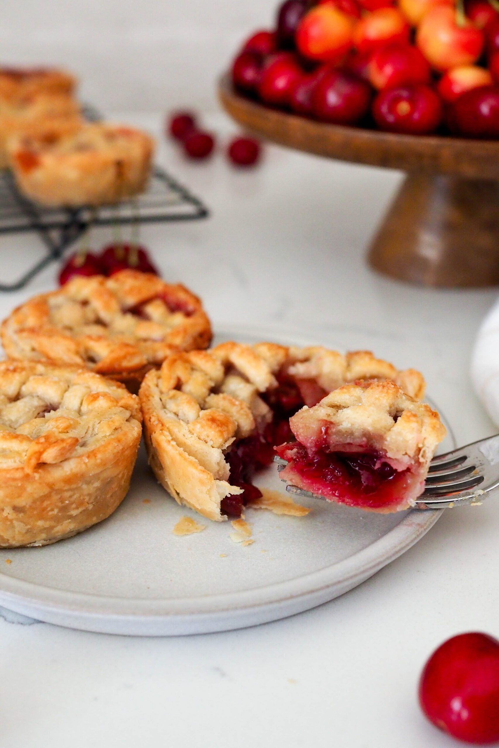 A fork pulls a piece of mini cherry pie off a plate.