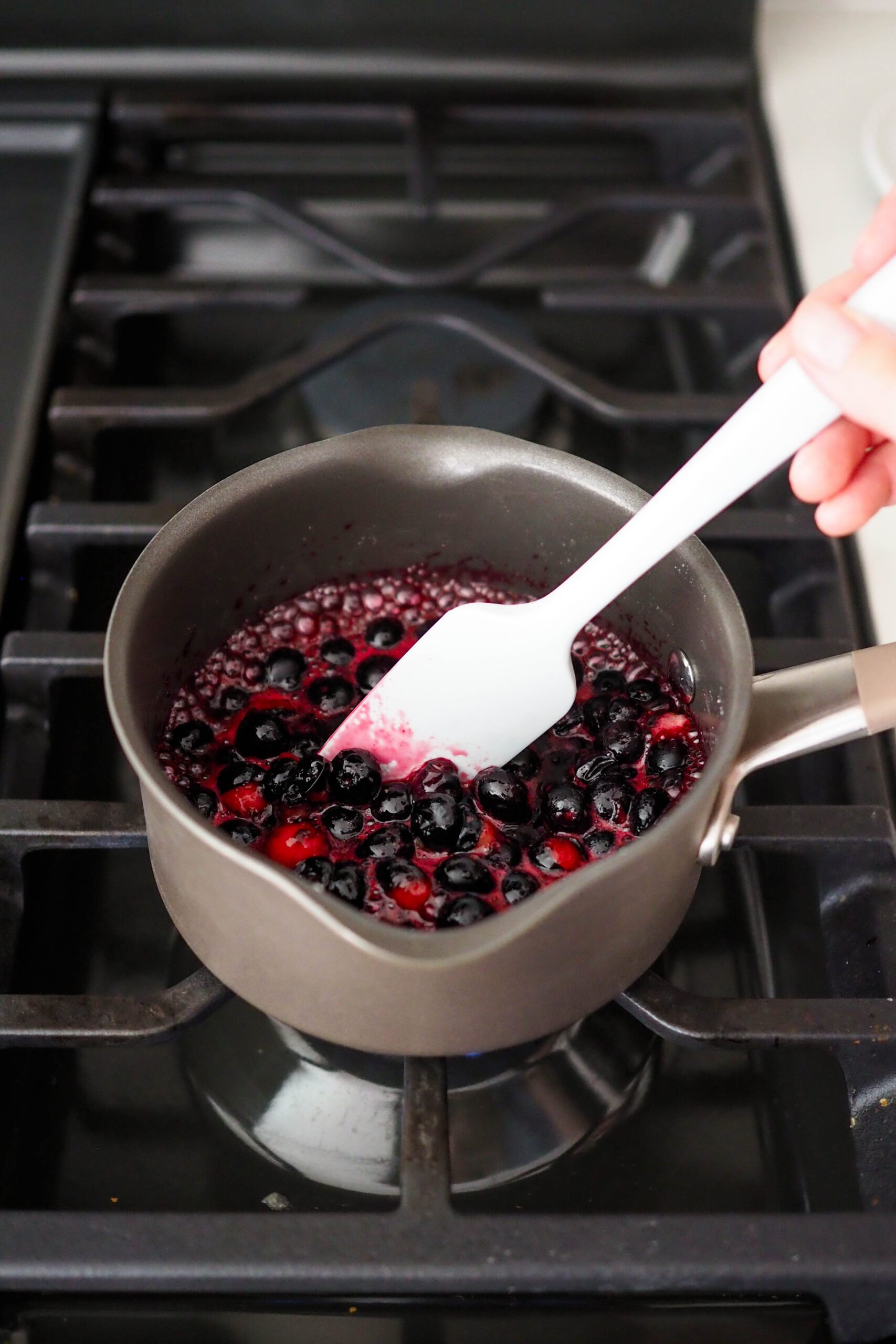 A spatula stirs down boiling blueberries in a small pot.