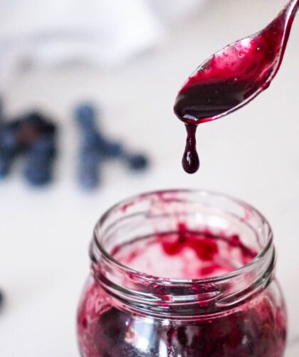 A spoon drips blueberry syrup into a jar.