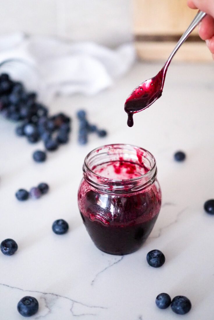 A spoon drips blueberry syrup into a jar.