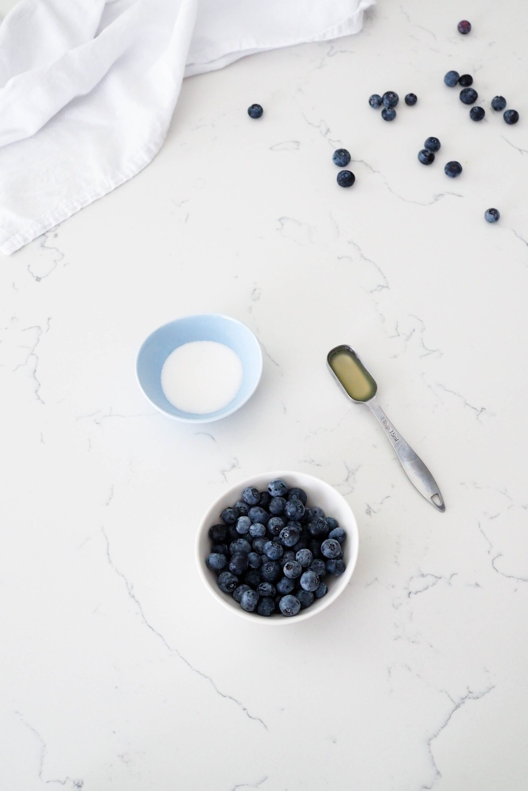Blueberries, sugar, and lemon juice on a marble counter.
