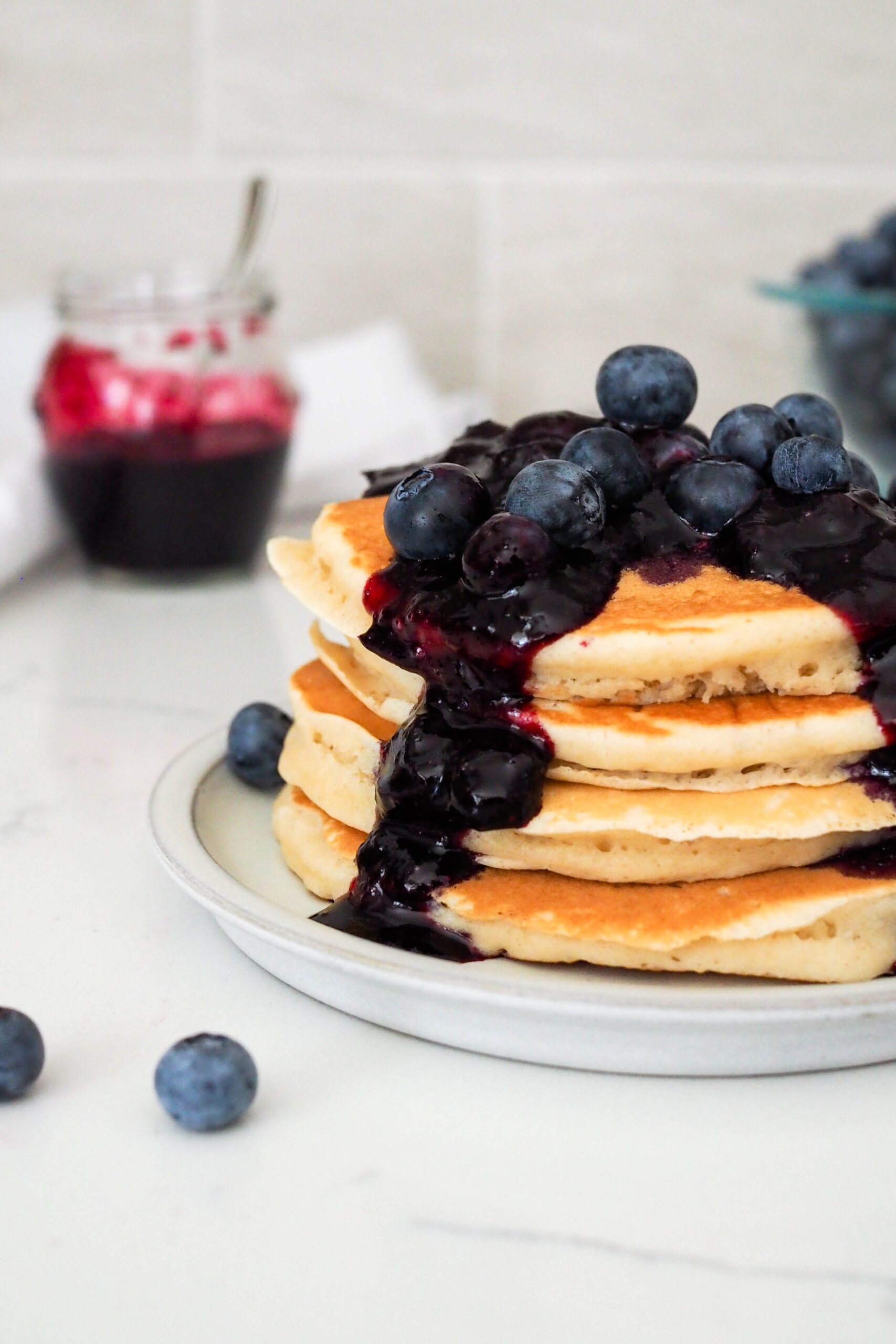 Chunky blueberry syrup drips down the side of a stack of pancakes.