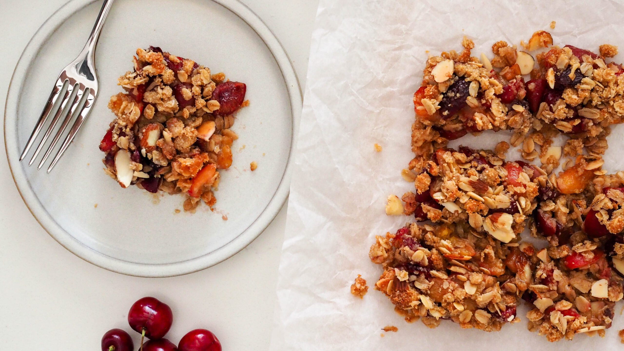 Overhead view of a gluten-free cherry almond crumble bar on a plate with the rest of the pan nearby.