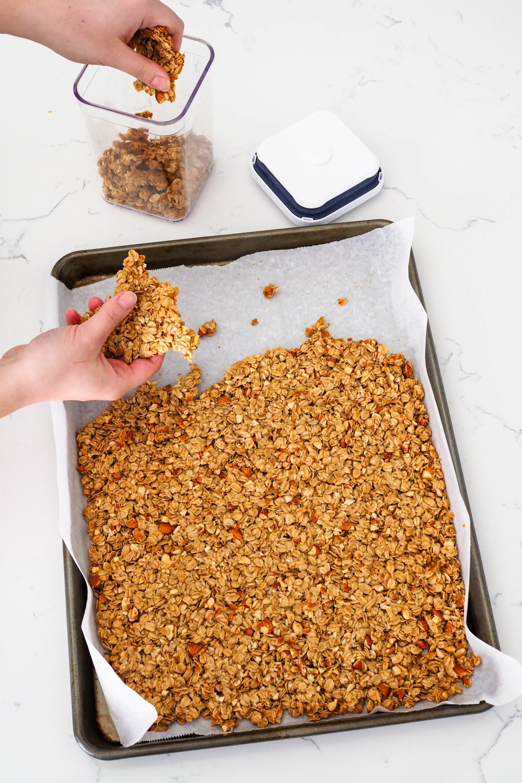 A hand breaks off a large triangle of granola from a pan.