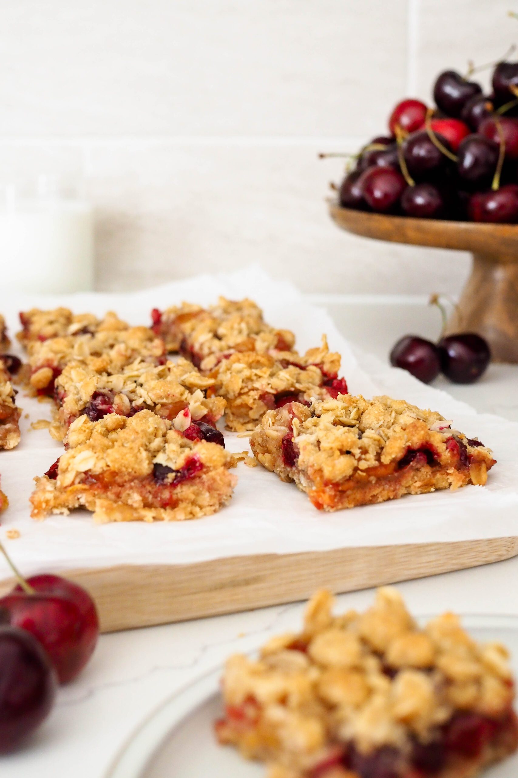A batch of cherry crumble bars on parchment near cherries.