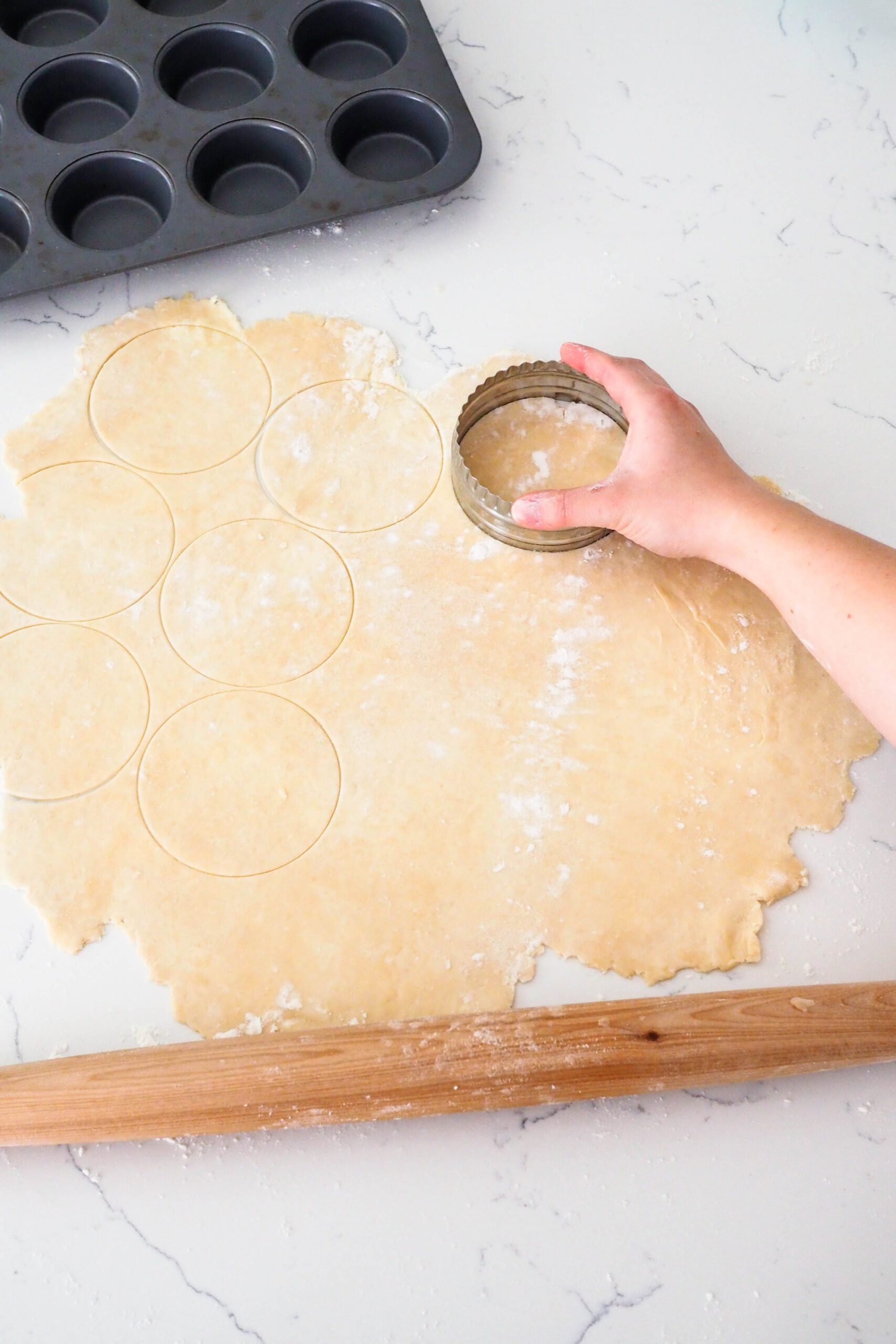 A hand cuts a 4" round in rolled out pie dough.