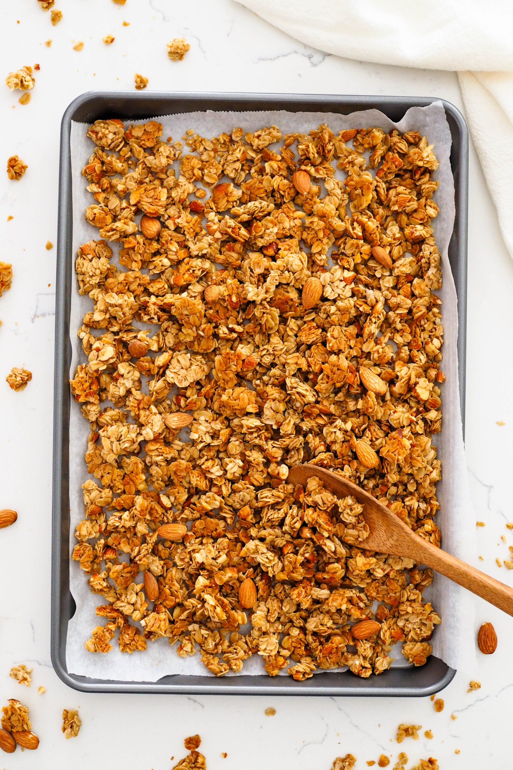 Vanilla almond granola in a baking sheet with a wooden spoon.