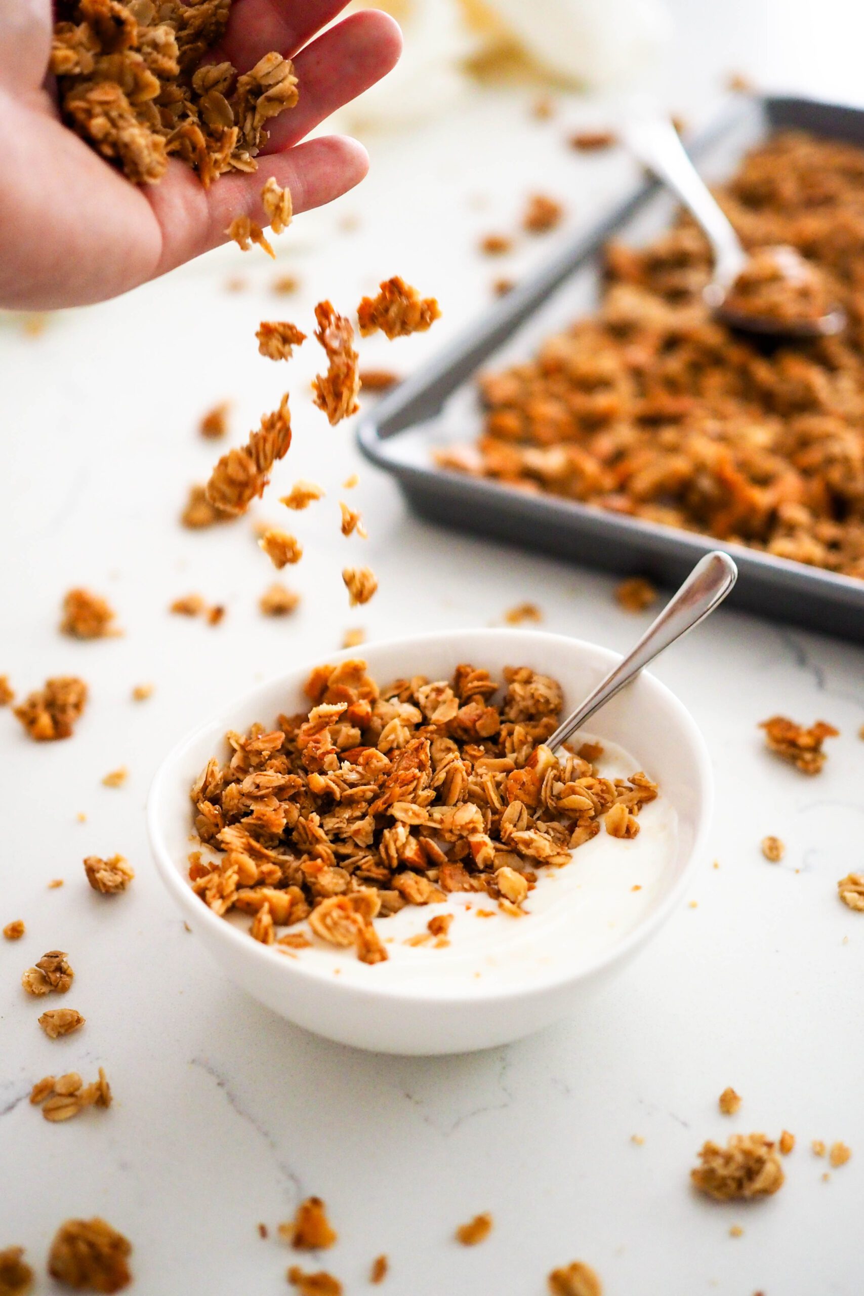 A hand sprinkles granola on top of a bowl of yogurt.