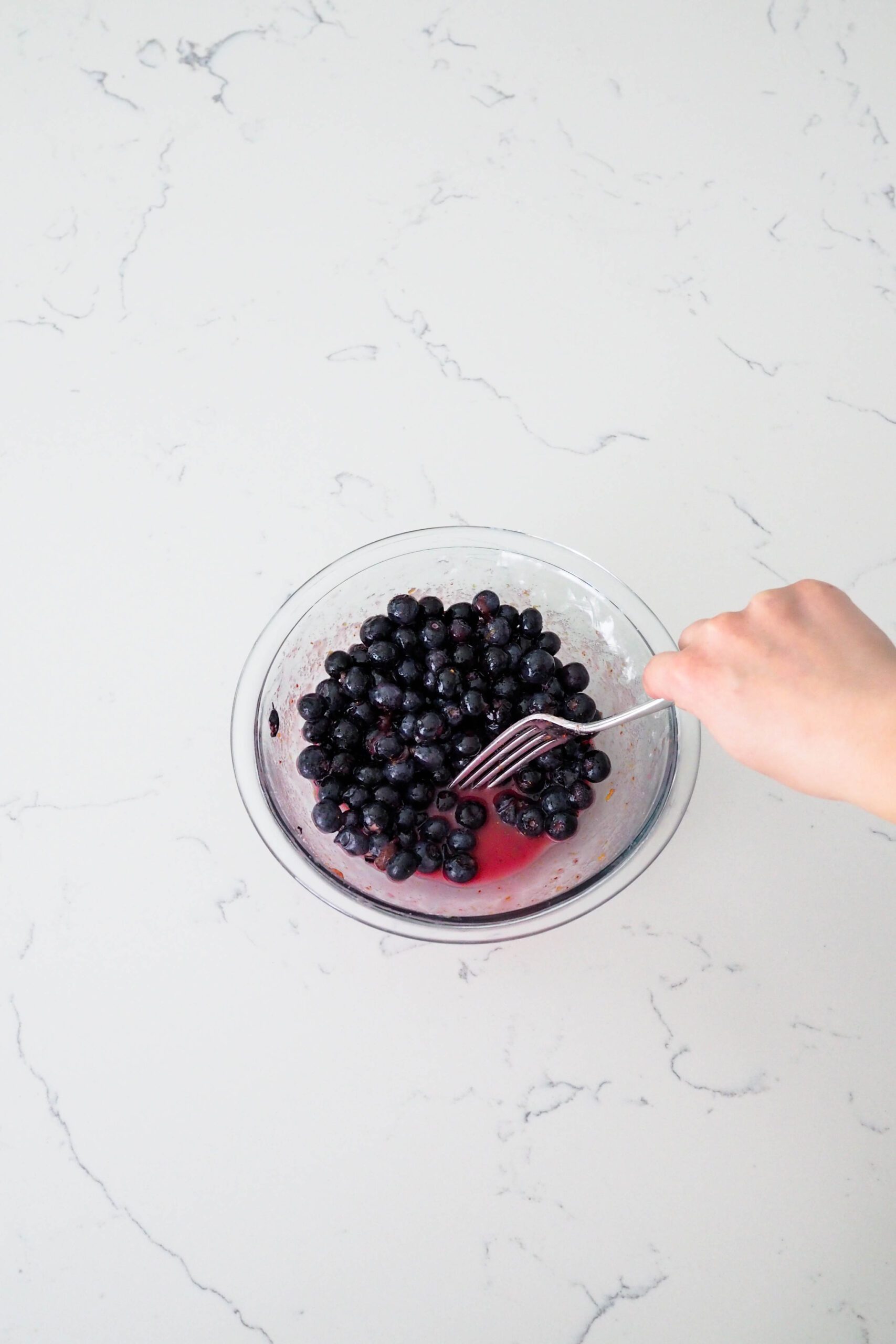 A fork pushes blueberries to the side of a bowl to show the pink liquid at the bottom.