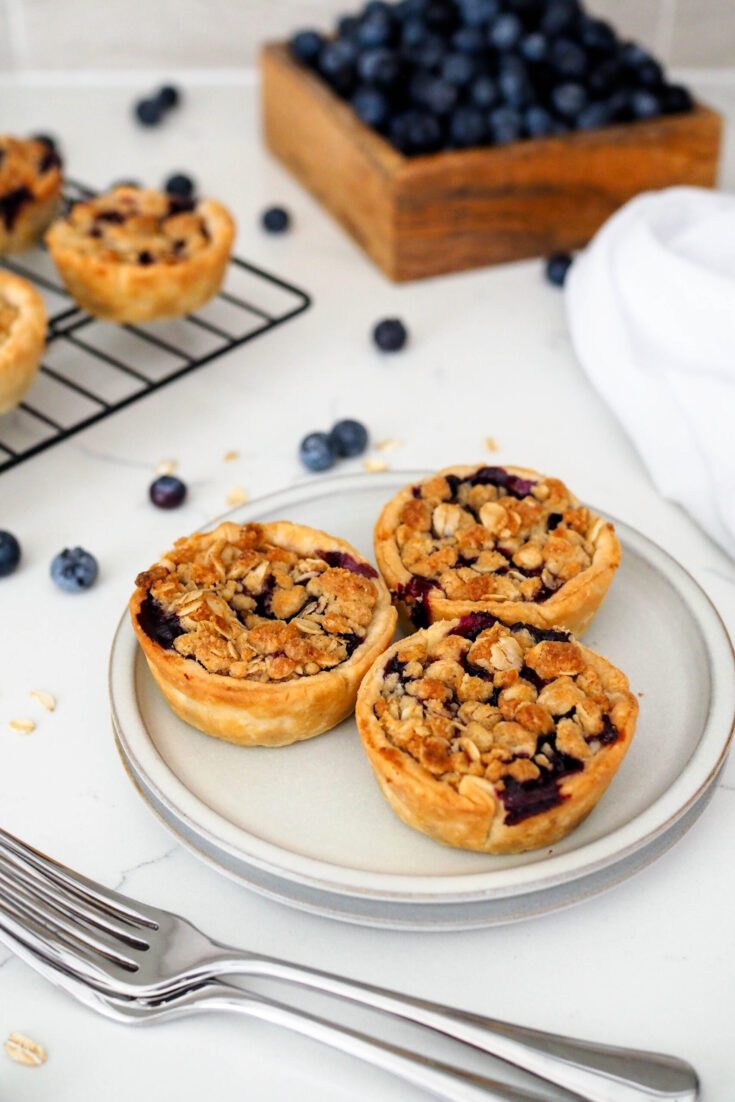 Three mini blueberry pies with a crumble topping on a gray appetizer plate.