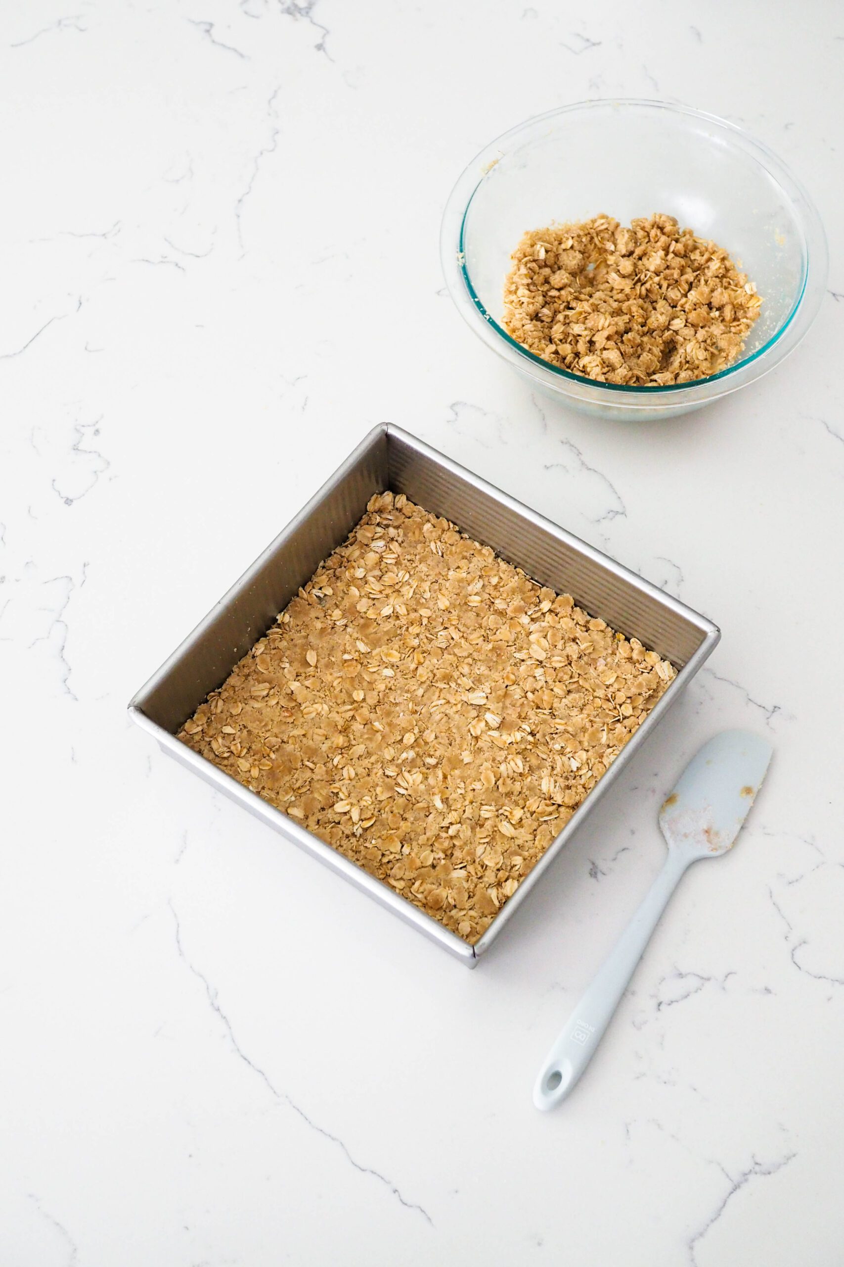 A square pan with oat crumble pressed into the bottom.