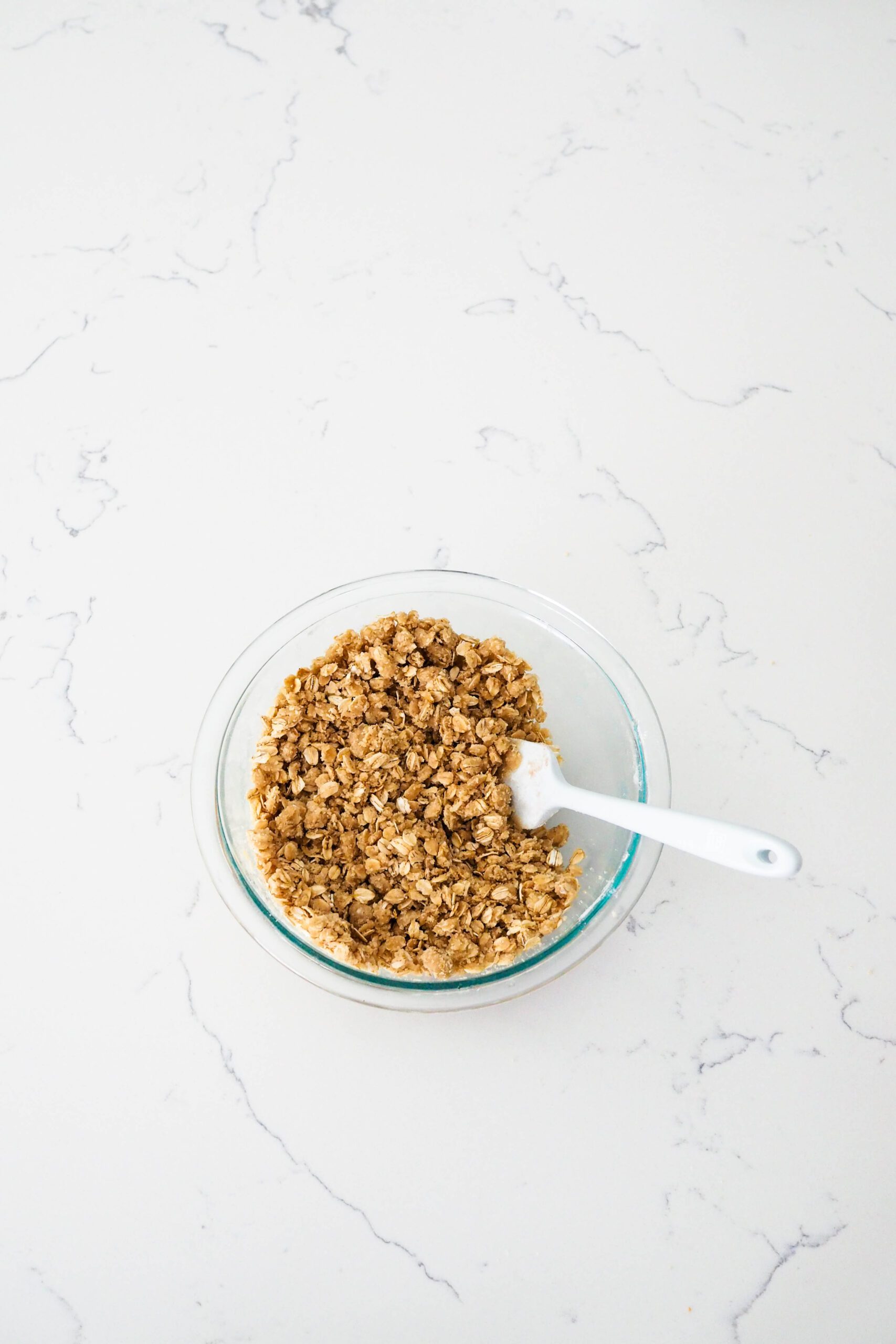 A bowl of oat crumble with a spatula sticking out.