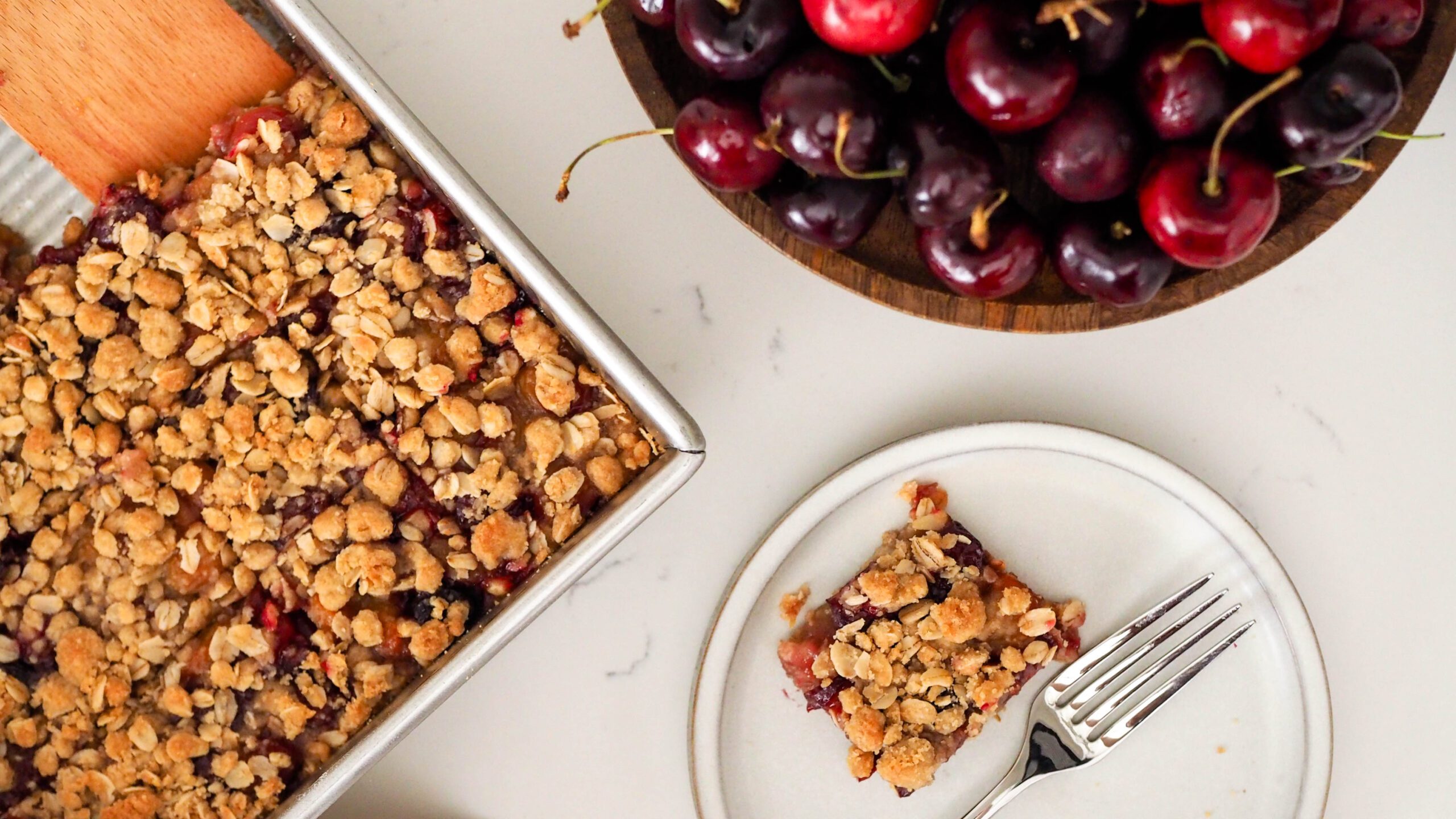 An overhead view of a pan of cherry crumble bars and nearby cherries.