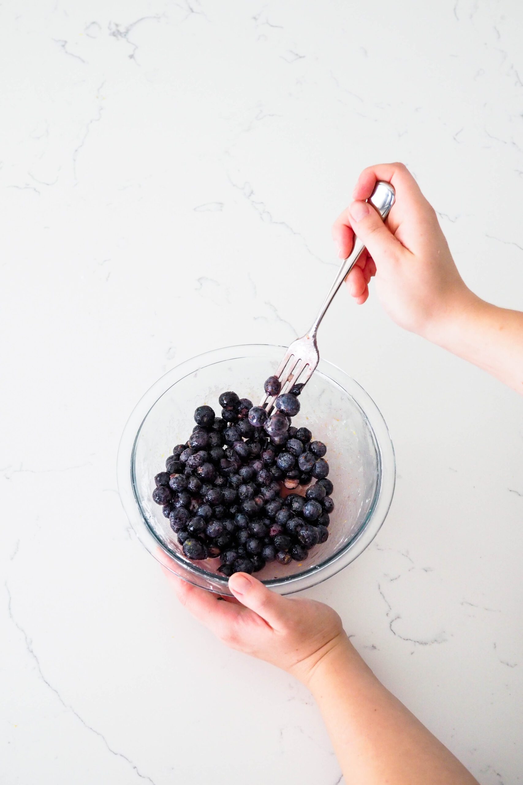 A hand pokes blueberries in a bowl with a fork.