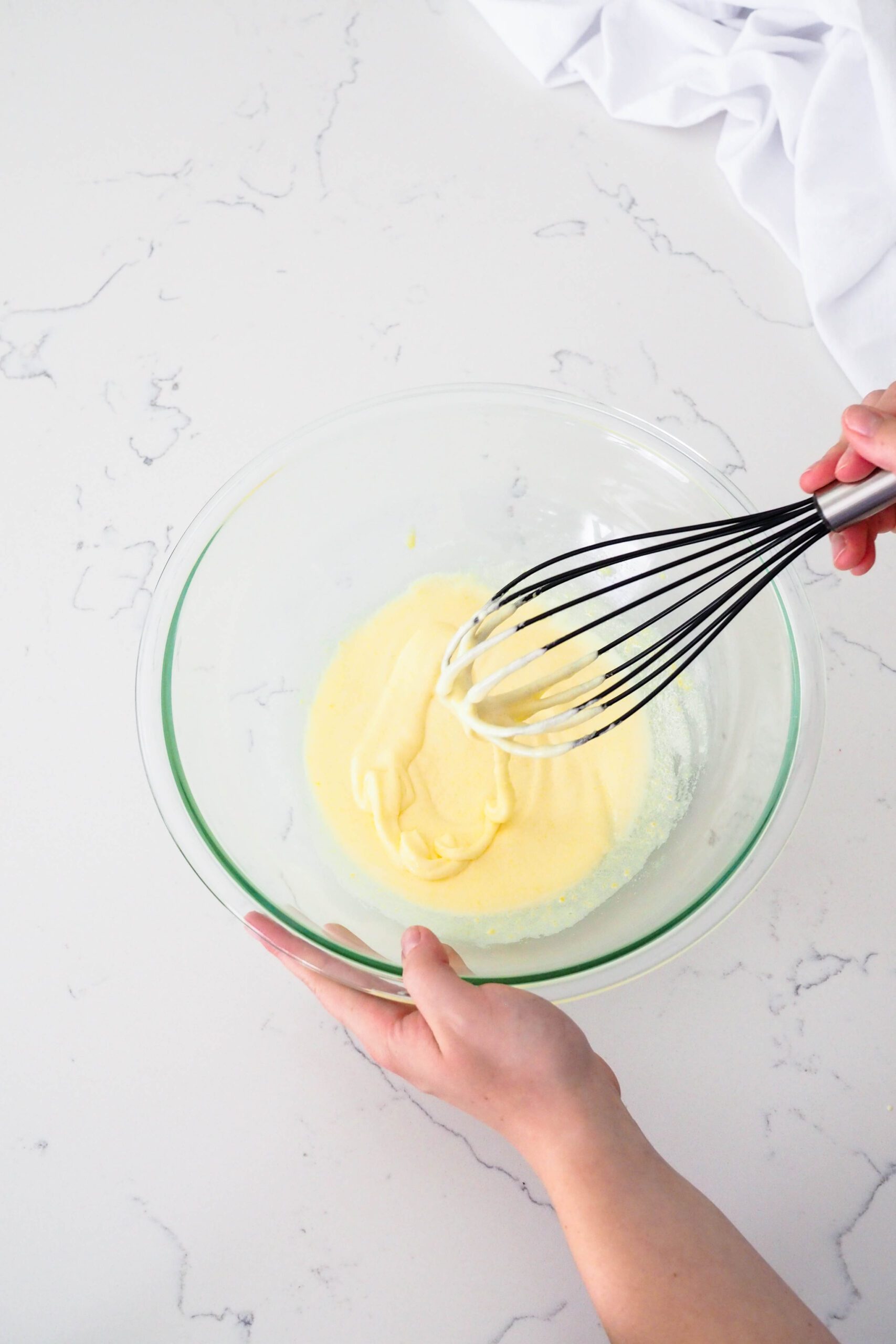 A ribbon of beaten eggs and sugar flows off a whisk in a bowl.