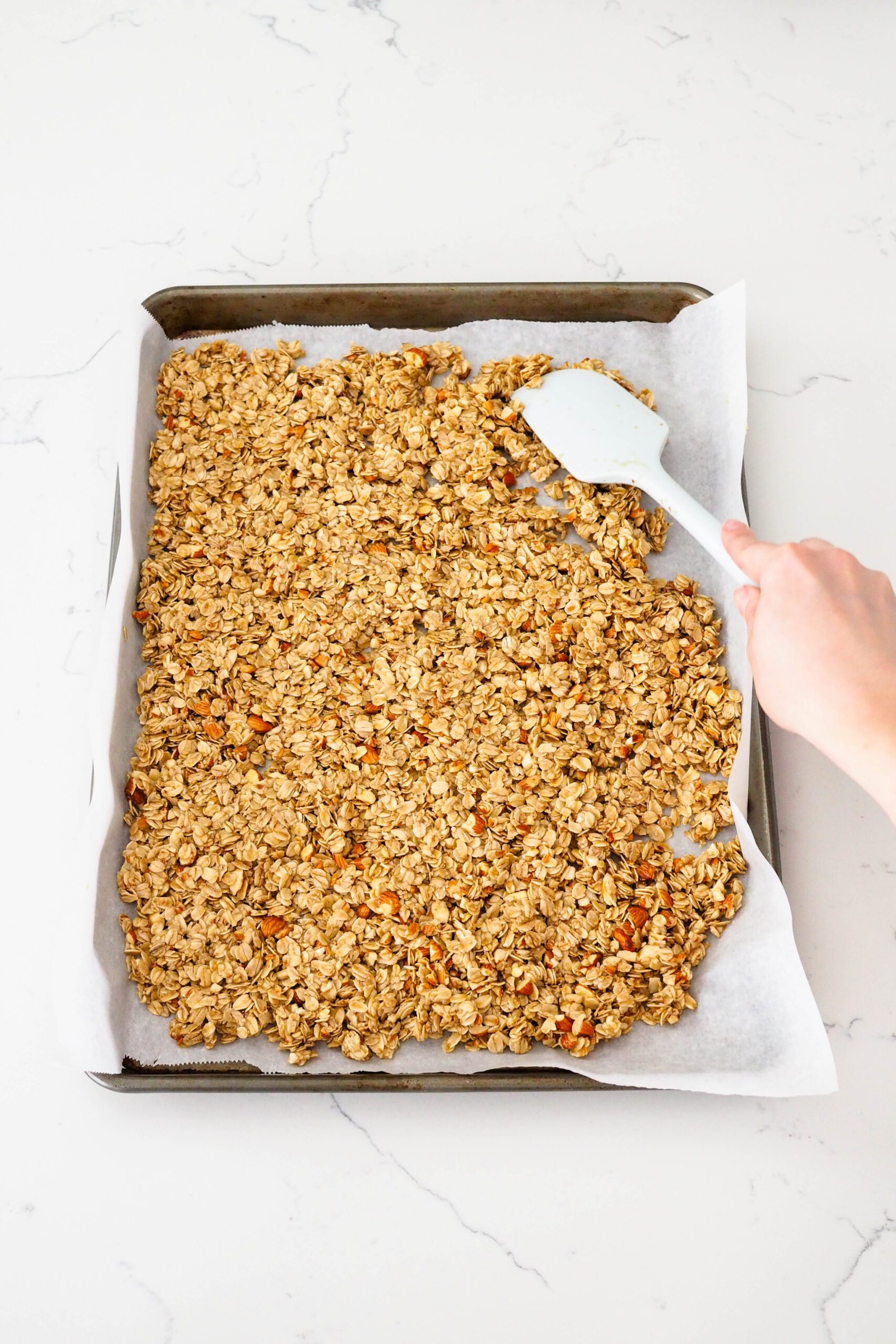 A spatula spreads out granola on a baking sheet.