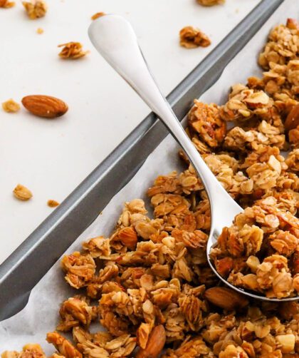 A silver spoon with vanilla almond granola on top of a pan of granola.