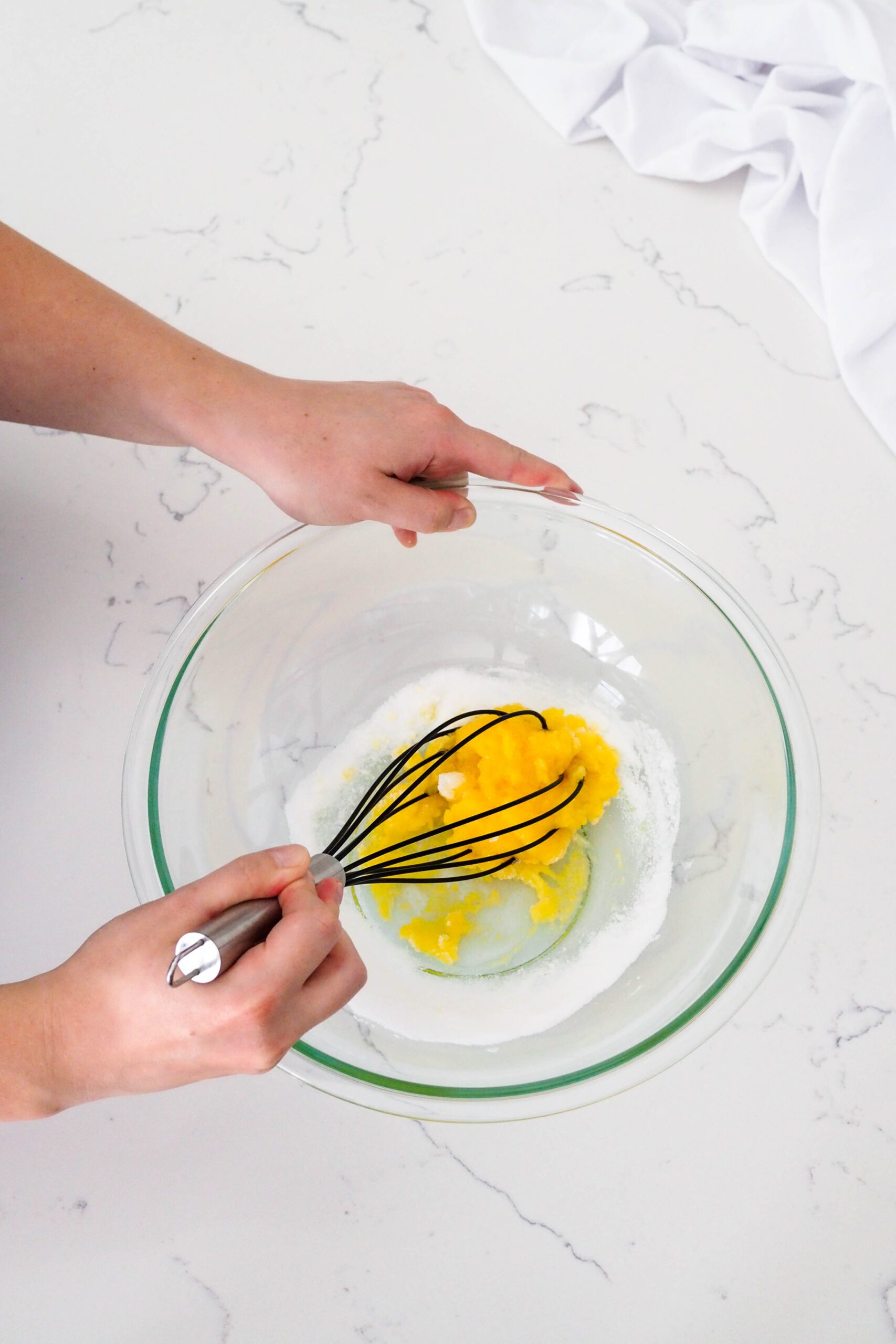 Two hands whisk together a dense and bright yellow mixture of egg yolks and sugar.