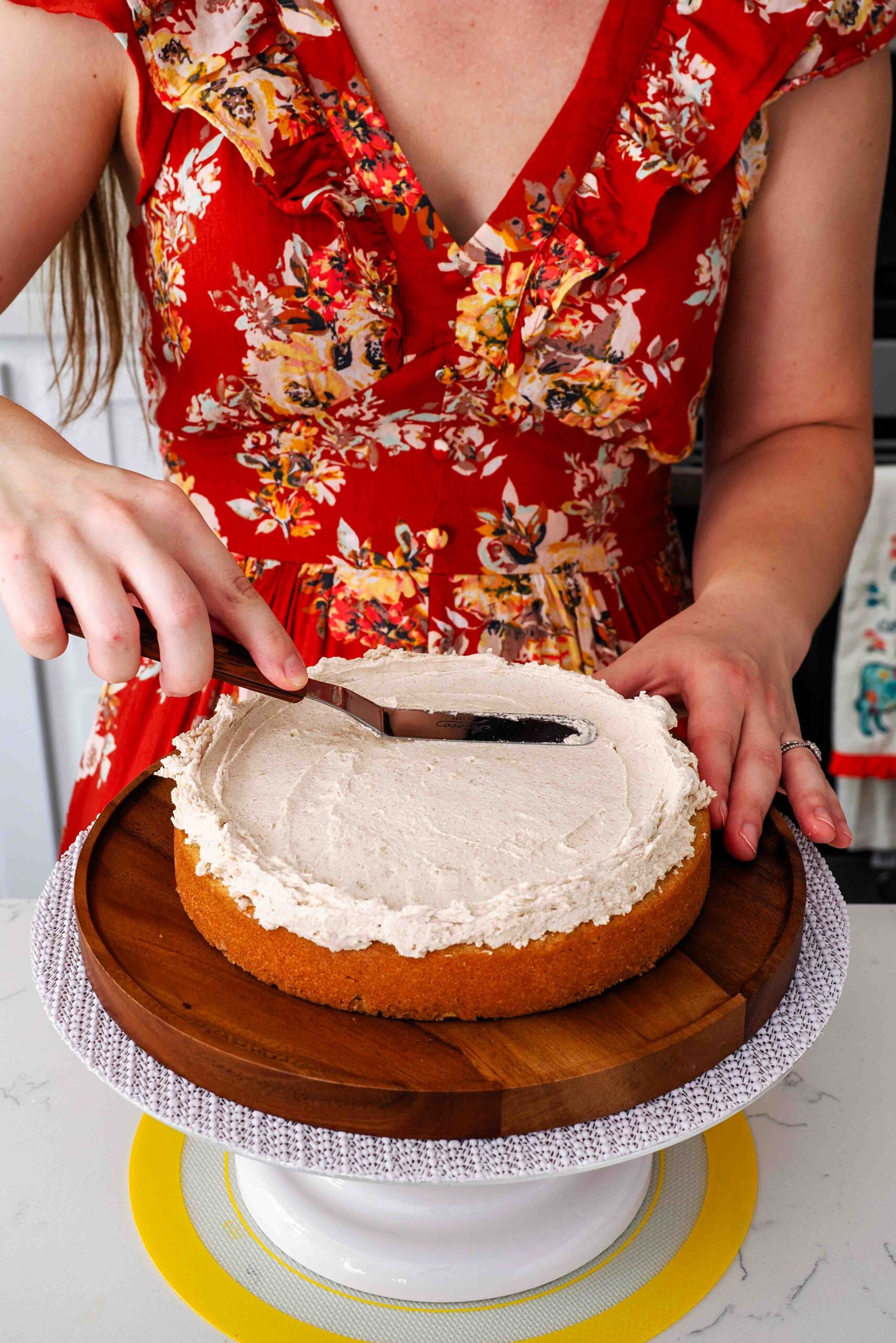 A woman smooths cinnamon buttercream on a cake layer with an offset spatula.